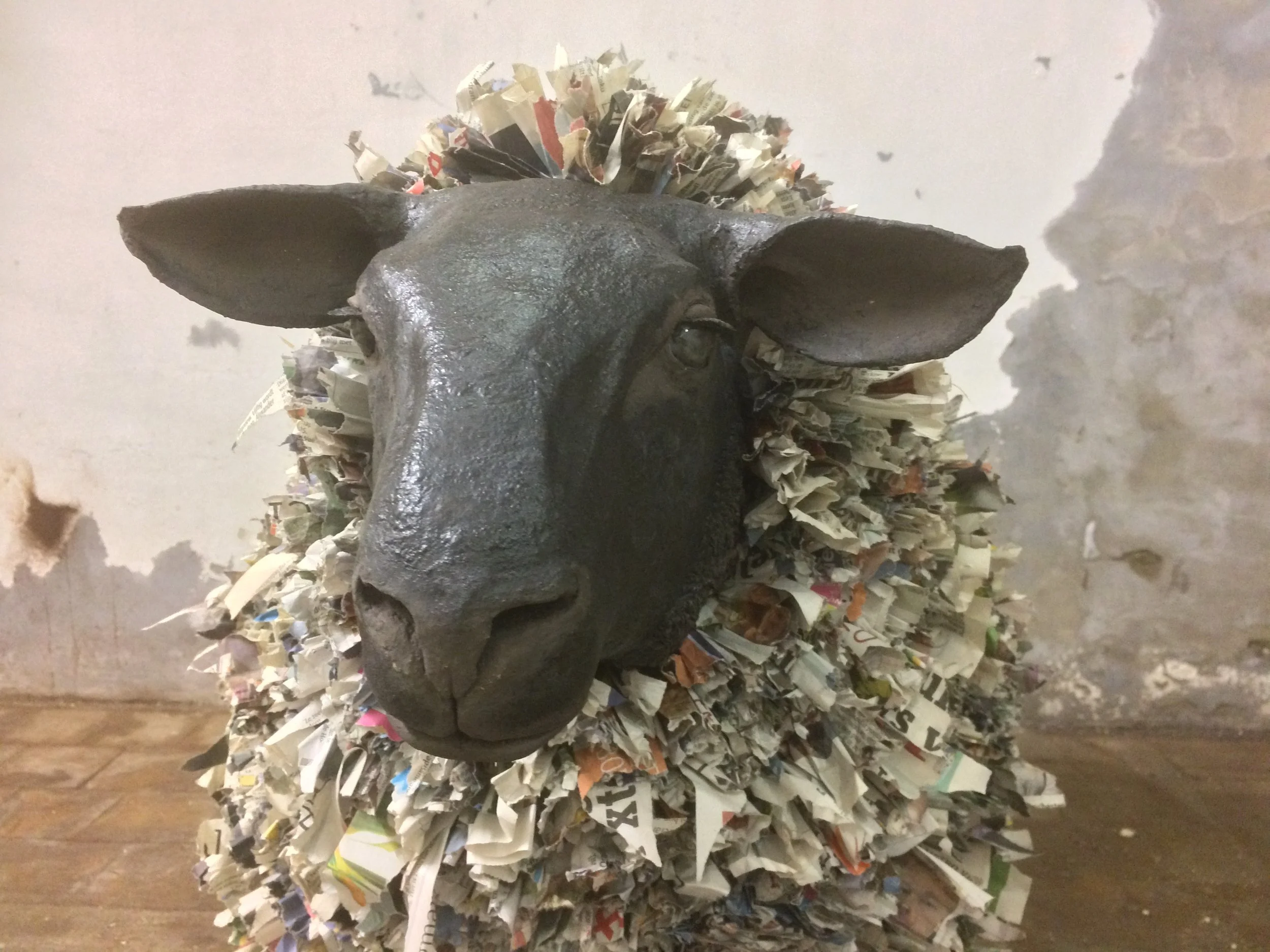 Art sculpture of a sheep with a head made of black material and a body covered in shredded newspaper.