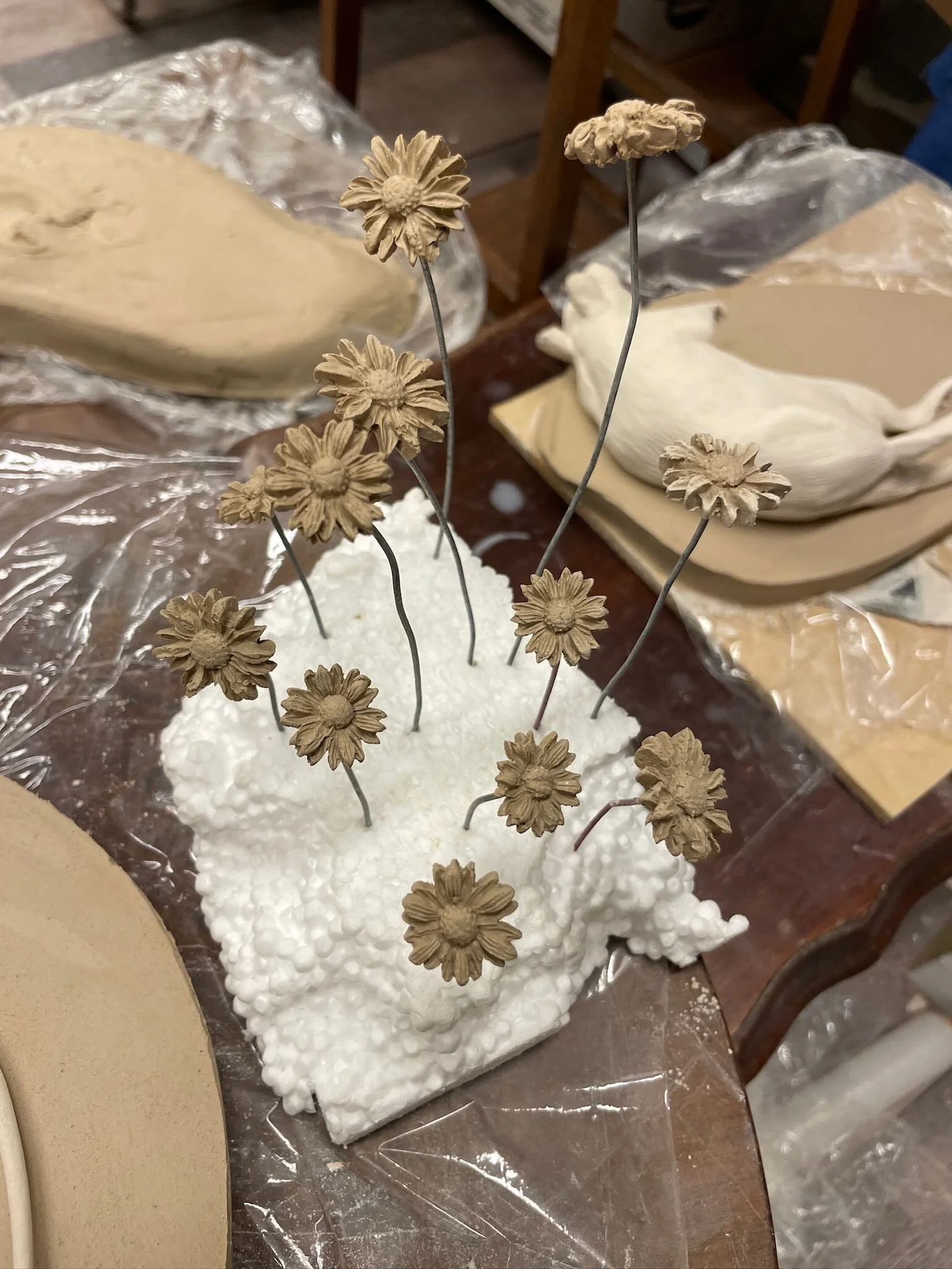 A white foam block with sunflower-shaped decorations on thin wires, resembling a bouquet of flowers.