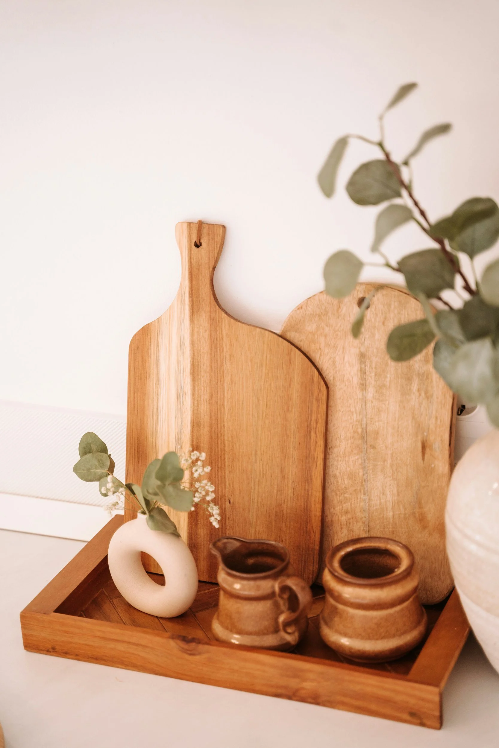 Decorative wooden tray holding vases, pottery, and greenery.