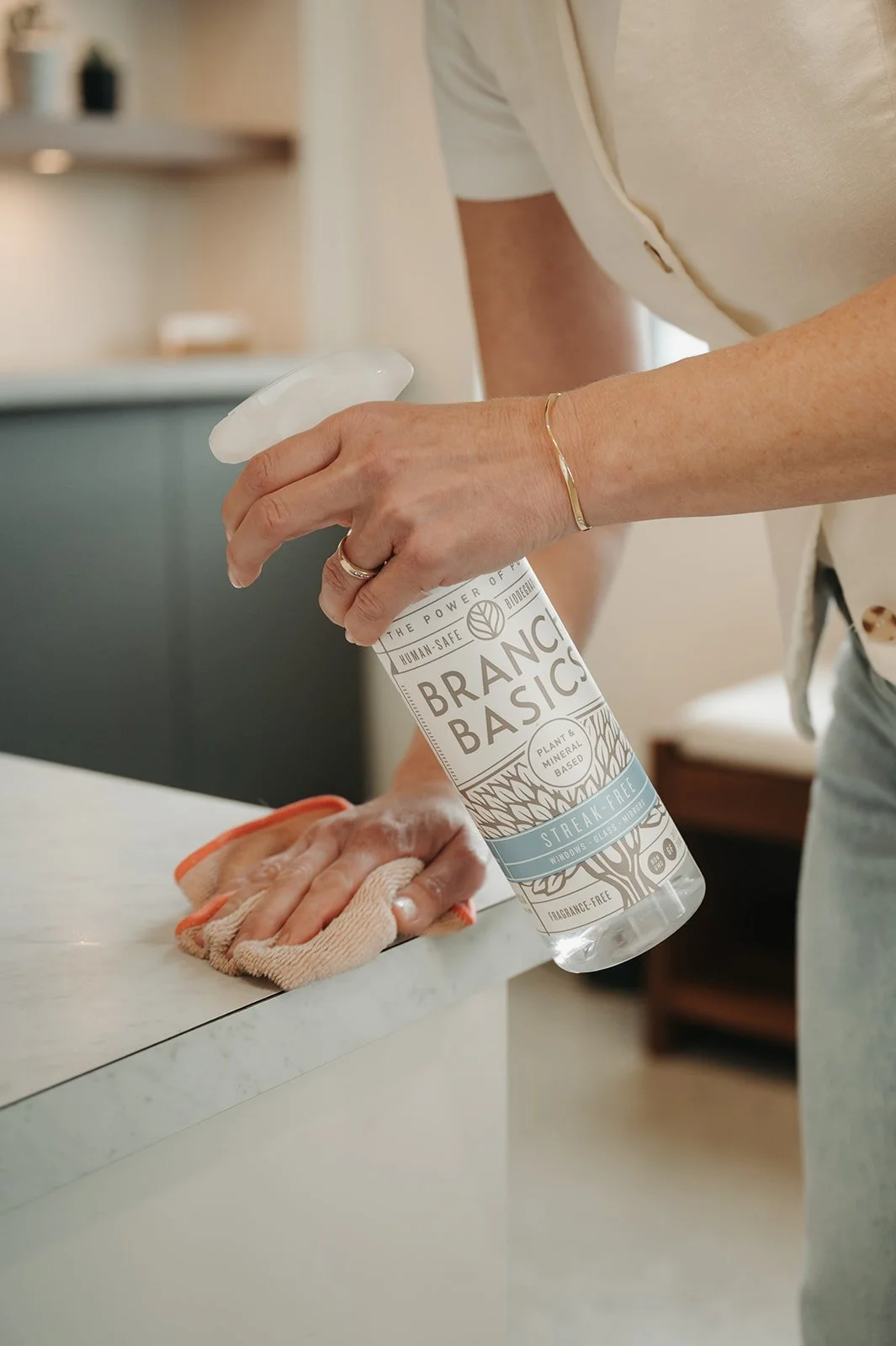 Person cleaning a countertop with a spray bottle and a microfiber cloth at Holm Collective, Lacombe AB.