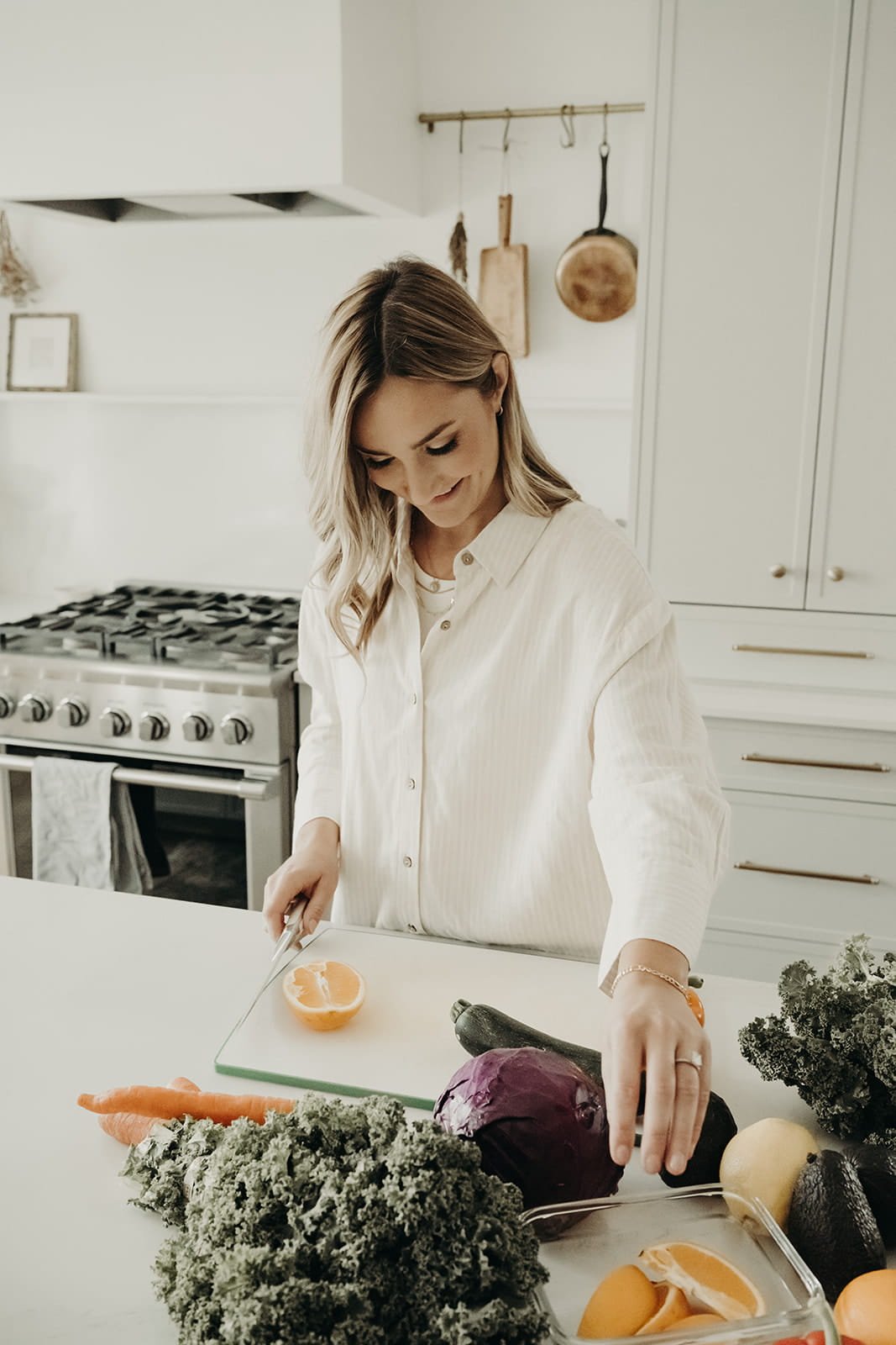Woman cutting an orange in a modern kitchen with vegetables on the counter.