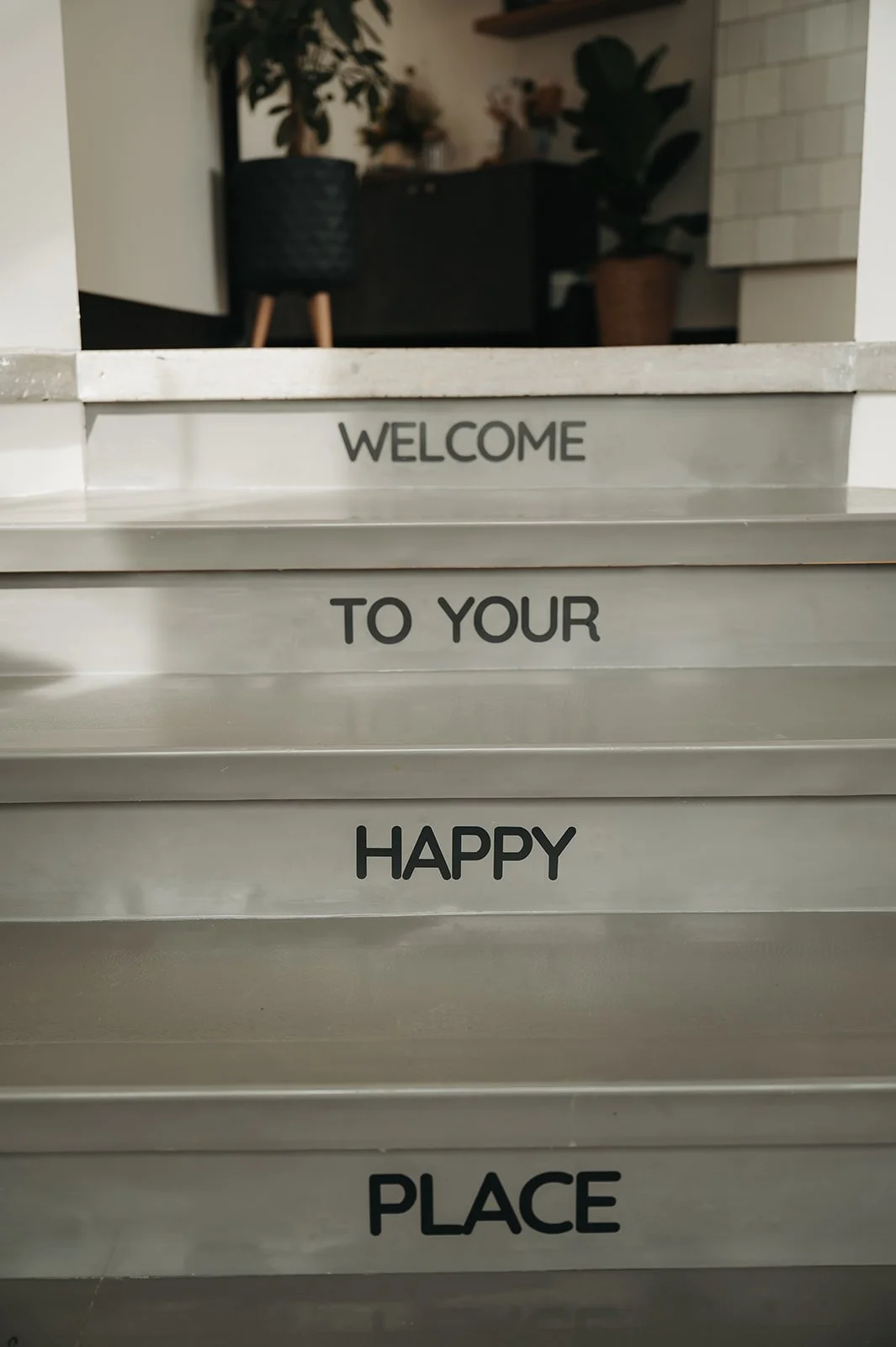 Metal stairs with black text reading, "Welcome to your happy place," in a modern indoor setting with plants at Holm Collective, Lacombe AB.