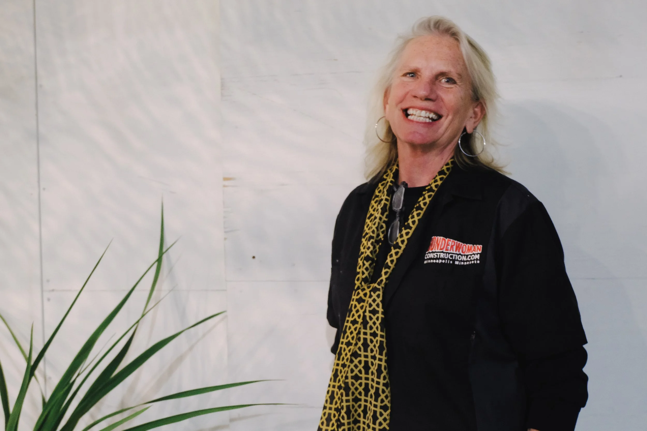 A smiling blonde woman wearing a black jacket with a