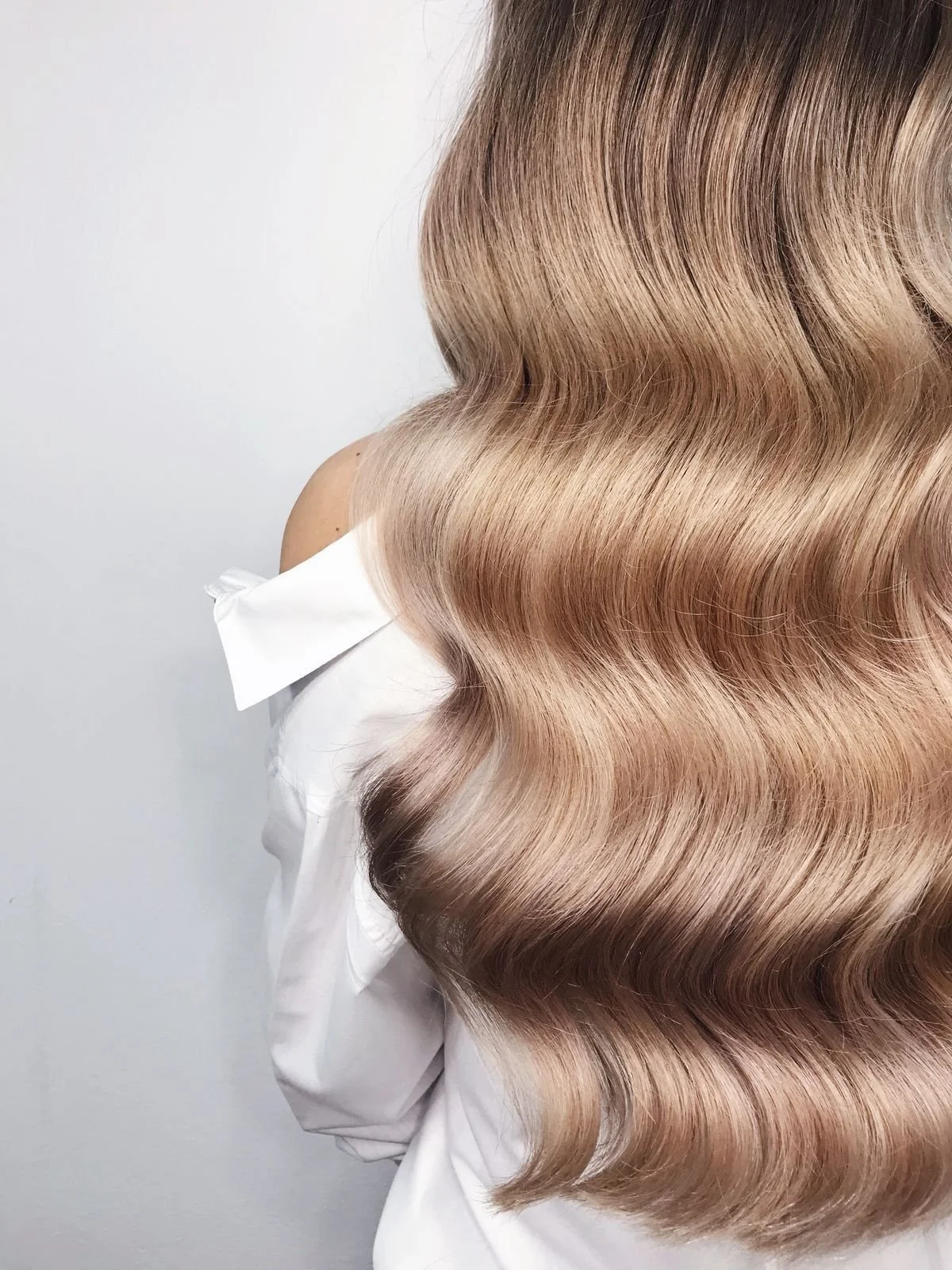 Close-up of a woman's wavy, blonde hair with a shiny, smooth texture, styled in soft, flowing waves.