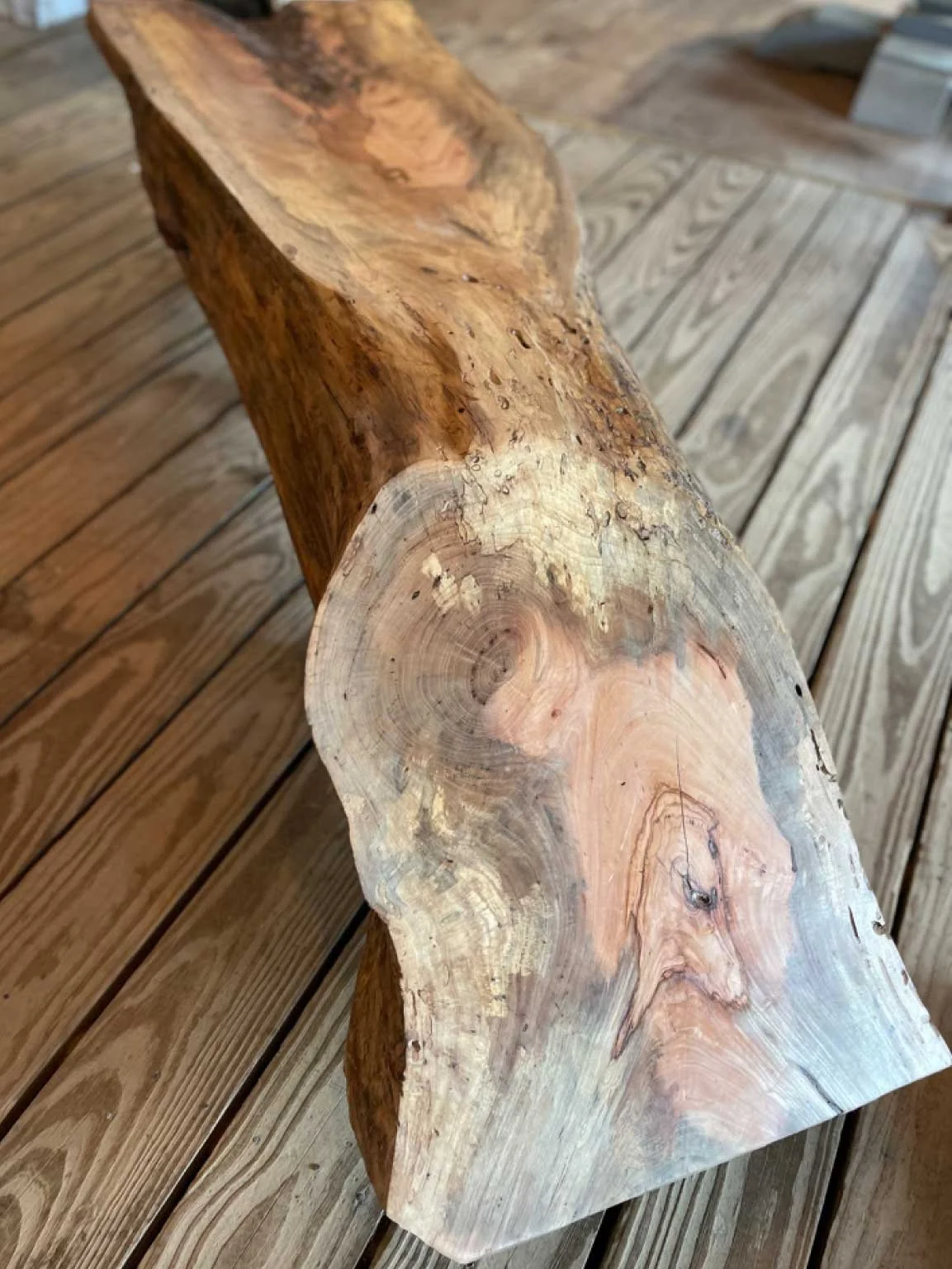 A wooden log with a natural edge, showing rings and knots, placed on a wooden deck.