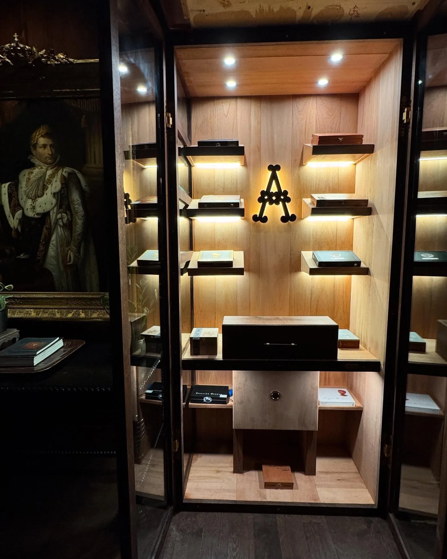 Wooden display cabinet with shelves holding books, illuminated by spotlights, with a large black letter 'A' in the center.