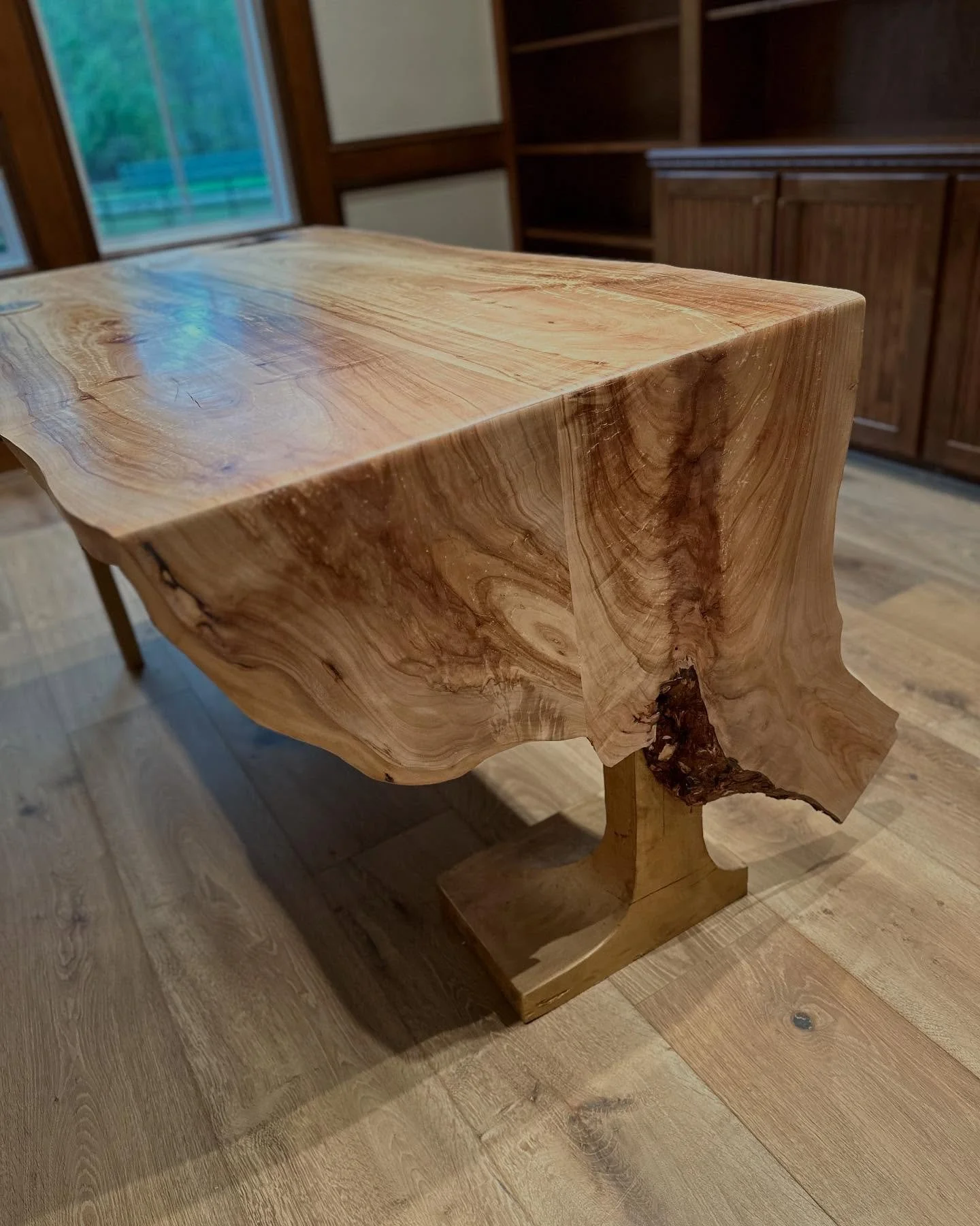 A close-up of a handmade wooden table made from a single slab of natural wood with a live edge, showing the wood grain and knots.