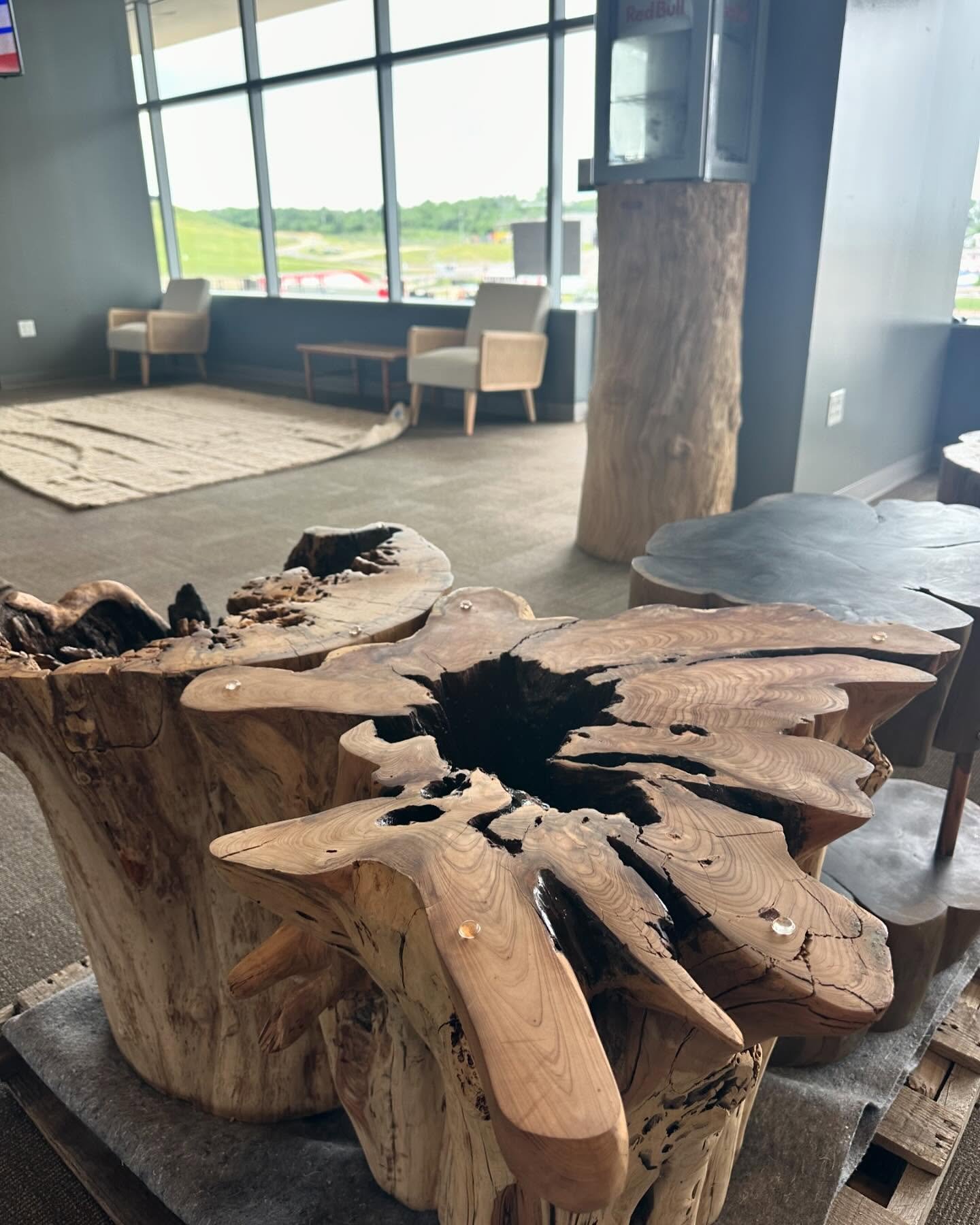 Close-up of a rustic wooden table with a natural and uneven surface, featuring black resin inlays in a modern space with large windows, chairs, and a carpet.