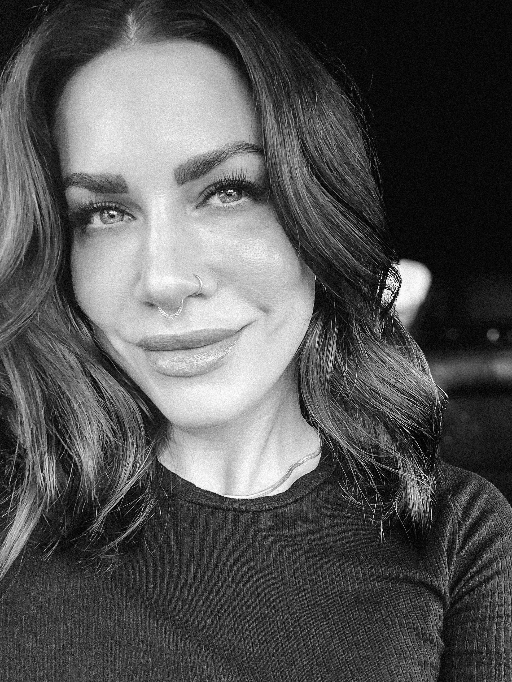 Black and white portrait of Mackenzie, founder of The Still Unsaid, with long wavy hair and a small smile.