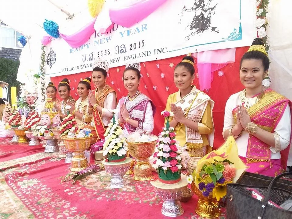 Women dressed in traditional attire performing a prayer during a festive celebration with offerings and floral arrangements on a decorated table.