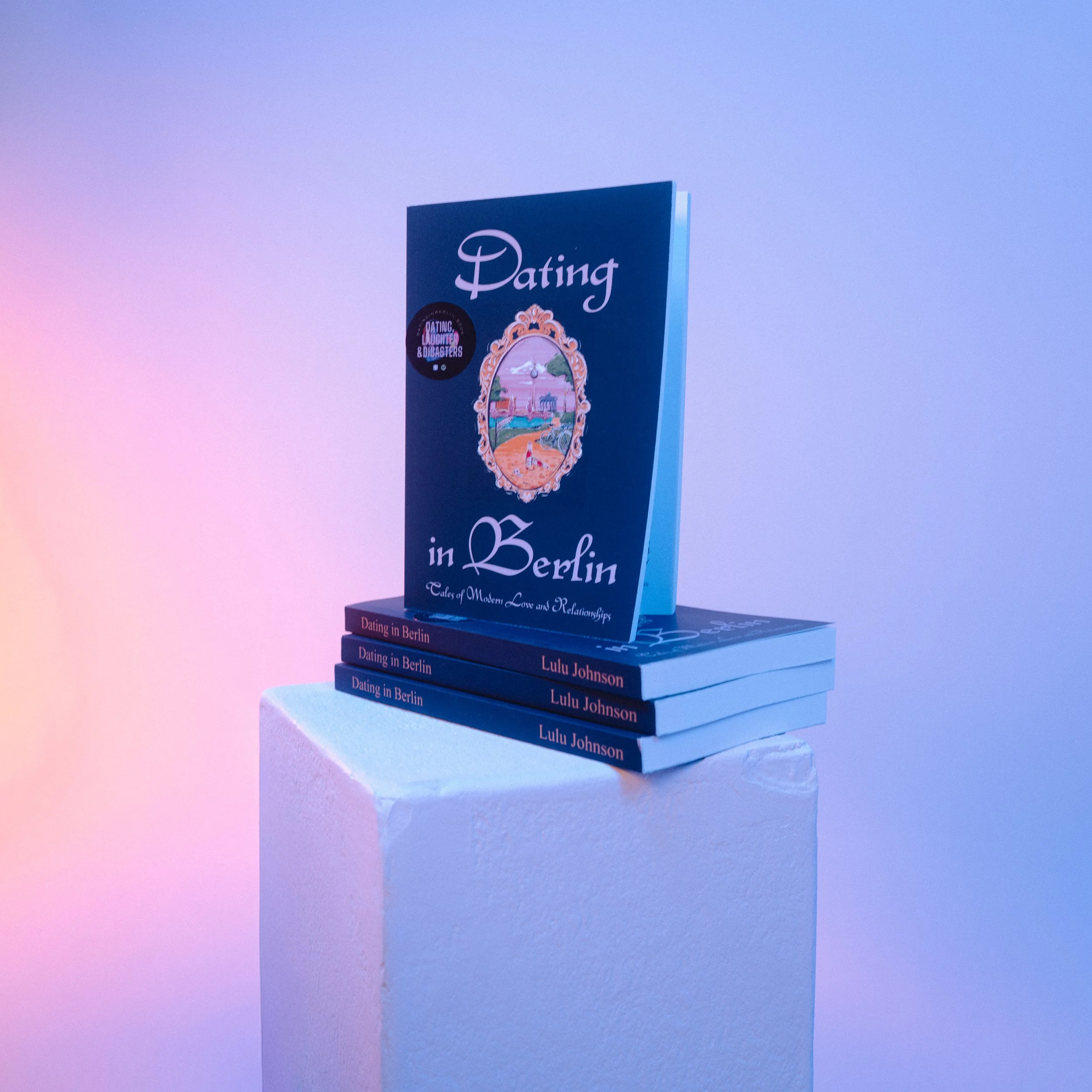 A stack of three books titled 'Dating in Berlin' by Lulu Johnson, with a single larger book on top titled 'Dating in Berlin: Tales of Modern Love and Relationships' displayed upright on a pedestal against a gradient background.