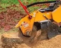 A yellow and black outdoor power tool, likely a concrete or rock saw, cutting through a large piece of wood or stone on the ground.