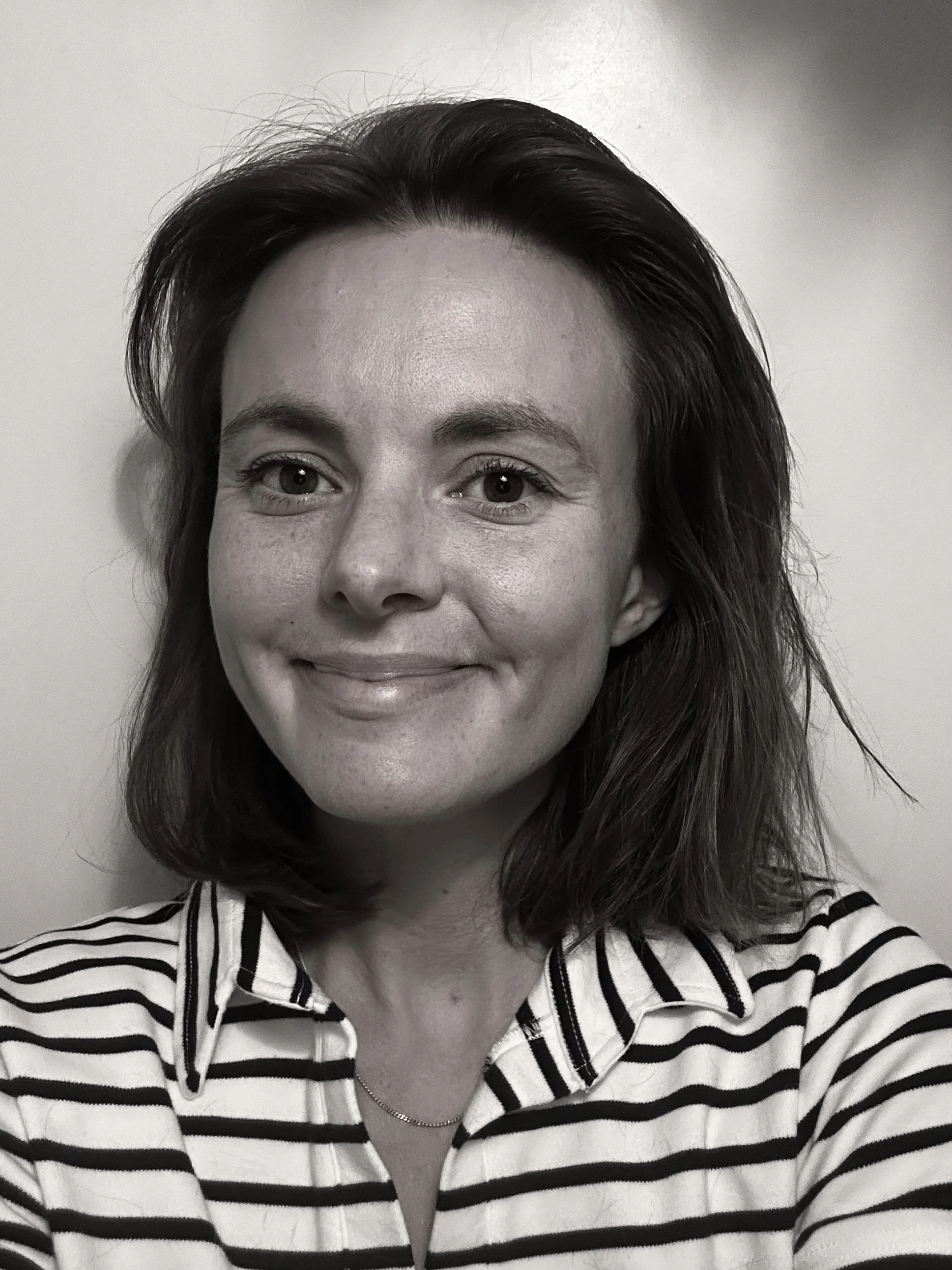 Svartvitt porträtt av en leende kvinna med mörkt hår, iklädd randig skjorta och kedja.