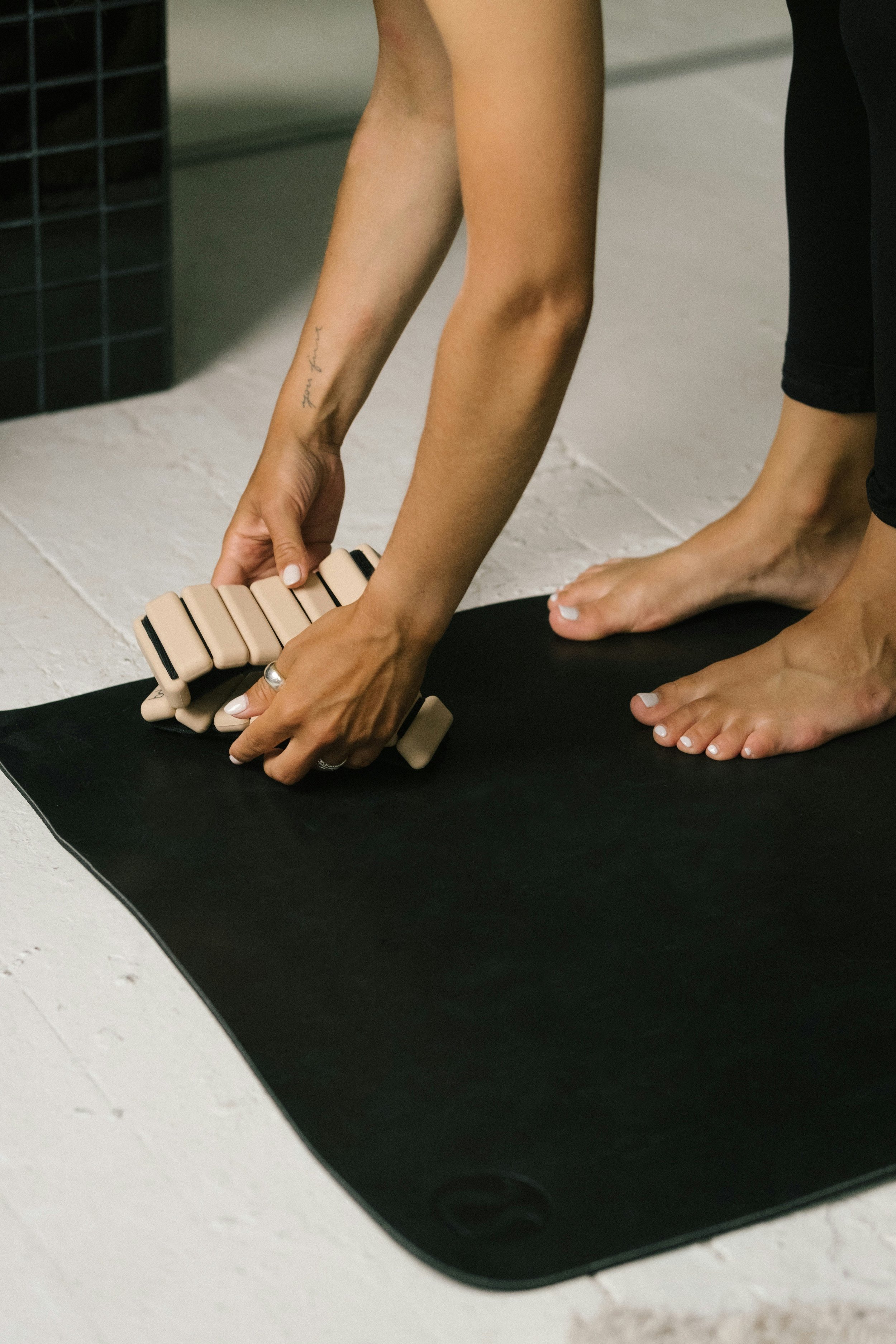 Person adjusting a yoga mat on a black exercise mat indoors.
