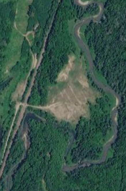 Aerial view of a winding river flowing through a forested area with an open grassy field in the center.