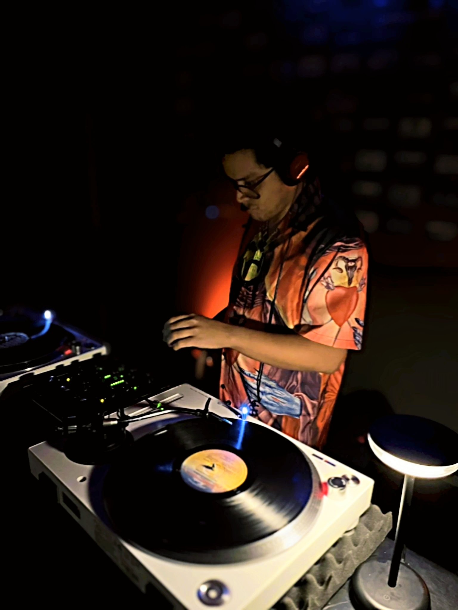 DJ con auriculares, mezclando música en un tocadiscos en un ambiente oscuro.