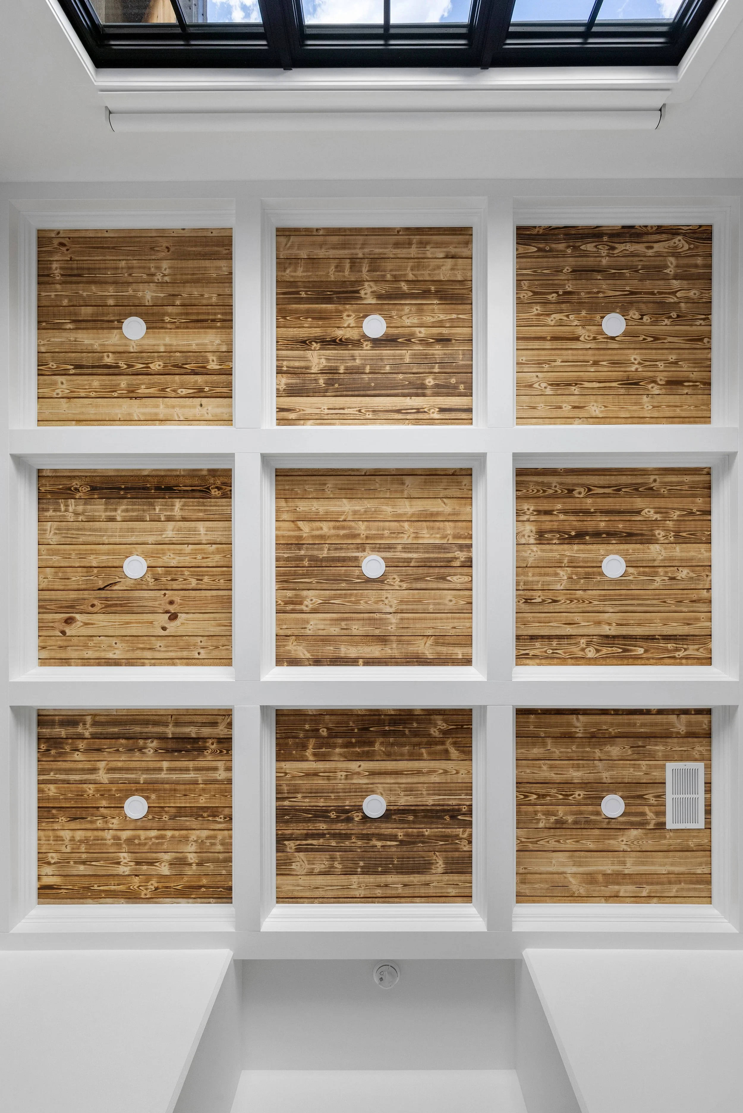 Interior view looking up at a ceiling with a skylight window, wooden panels, white framing, and circular vents