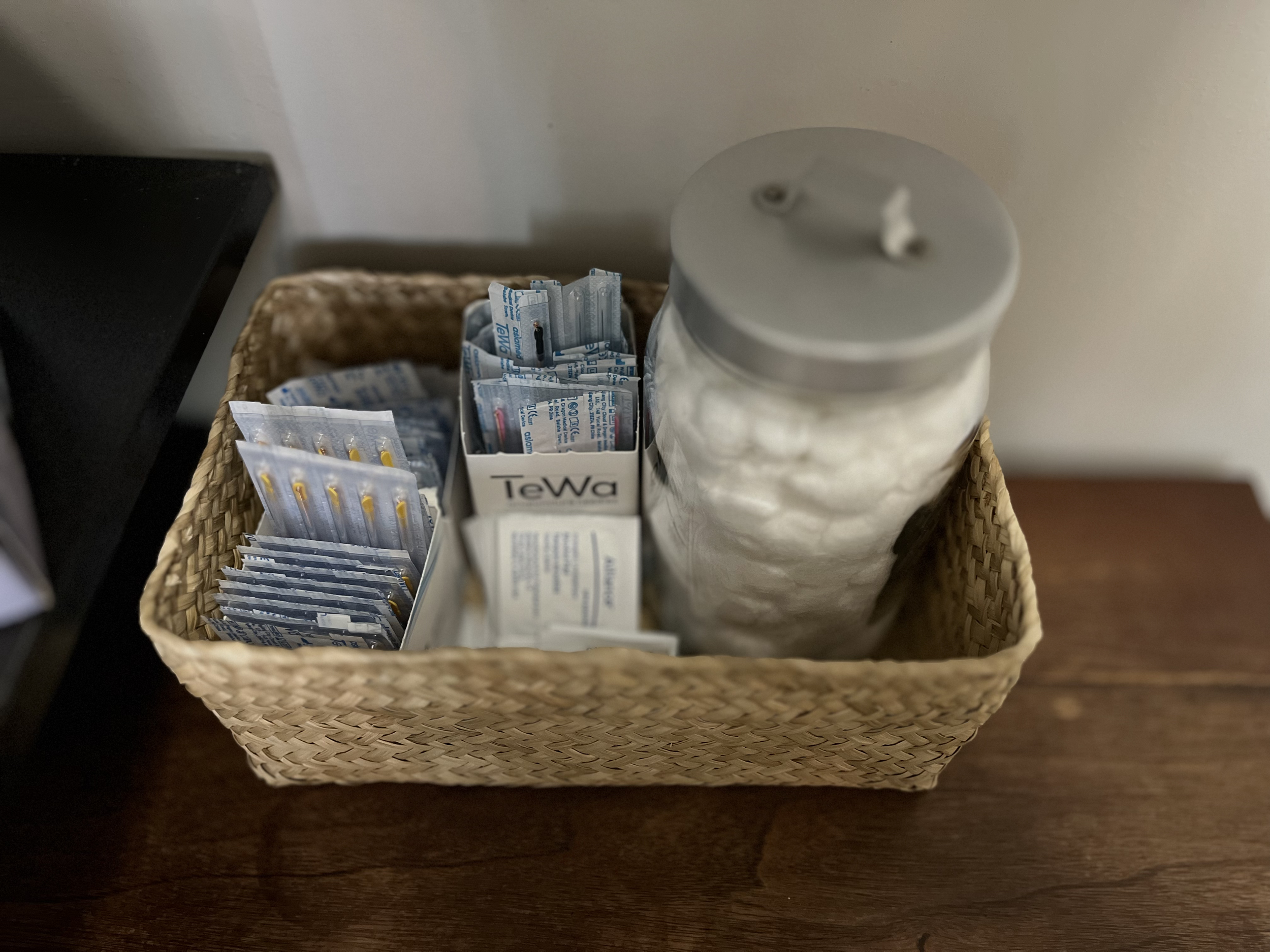 Wicker basket with various tea bags and a jar of cotton balls on a wooden surface
