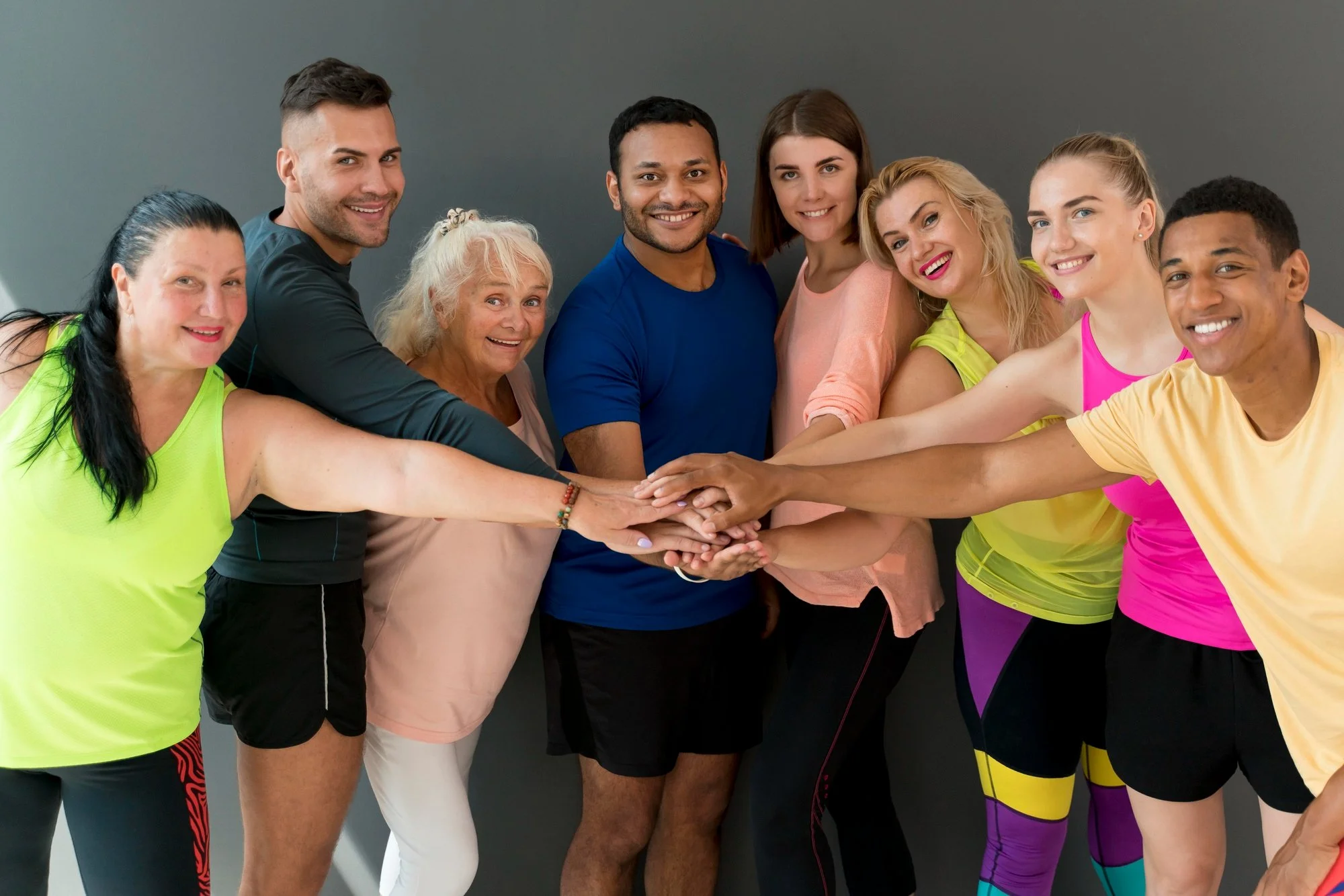 Group of diverse young adults in athletic clothing putting their hands together in a team huddle indoors.