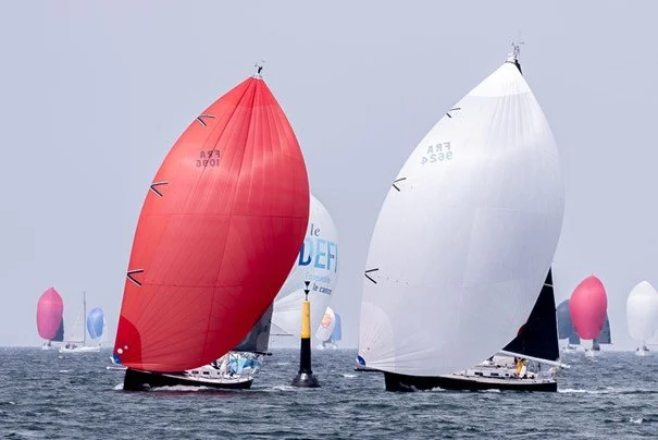 Voiliers en course dans la mer, avec plusieurs voiles colorées, principalement rouge et blanche, sous un ciel nuageux.