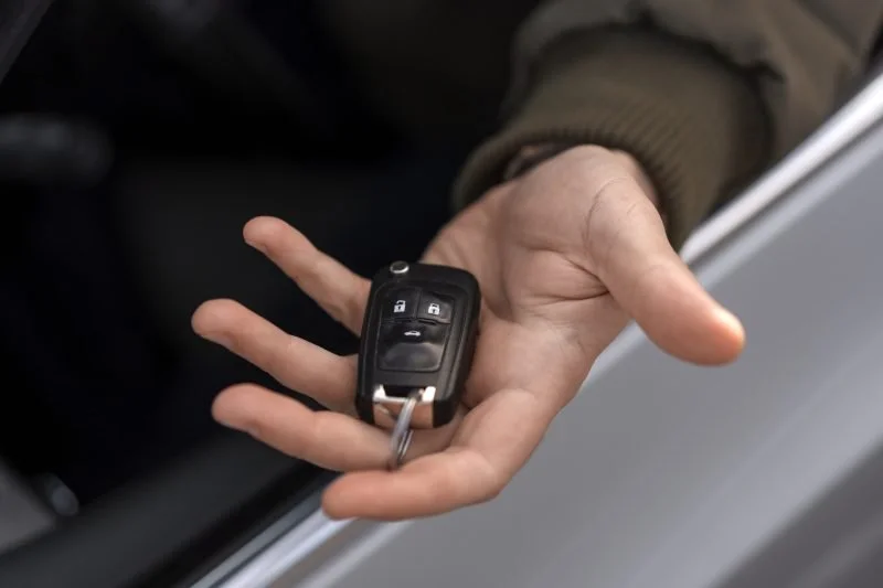 Hand holding a car key fob with lock and unlock buttons.