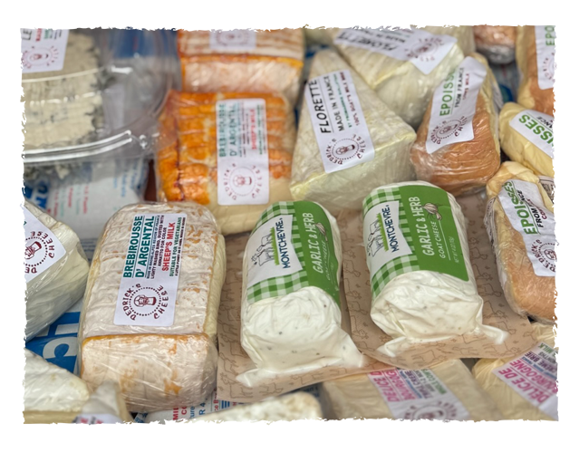 Assorted Brie and cream cheese spreads in individual plastic wrappers with labels, including garlic and herb flavor, placed on a flat surface.