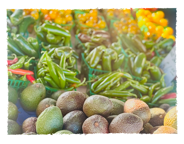 Fresh green avocados, green chilies, and yellow tomatoes at a produce market stall.