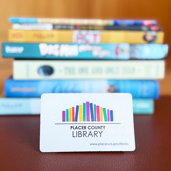 Placer County Library card in front of a stack of children's books on a wooden surface.