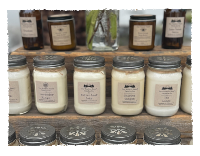 Multiple candles in glass jars with metal lids, labeled with scents like Lavender Flower, Fallen Leaf Lake, Shirley Canyon, and The Lodge, arranged on a rustic wooden shelf.