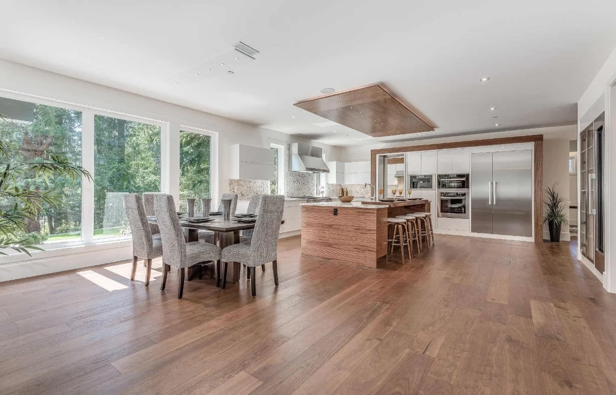Bright, modern kitchen with large windows, wooden floor, white cabinets, and a kitchen island with bar stools.