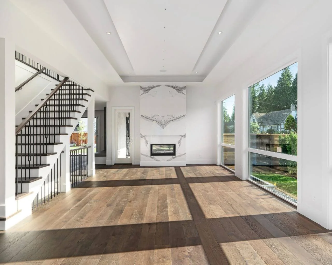 Bright, open living room with large windows, wooden floors, and a modern fireplace with marble accents.