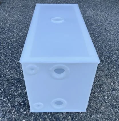 Large white styrofoam cooler on asphalt surface, with circular openings on its top and side.