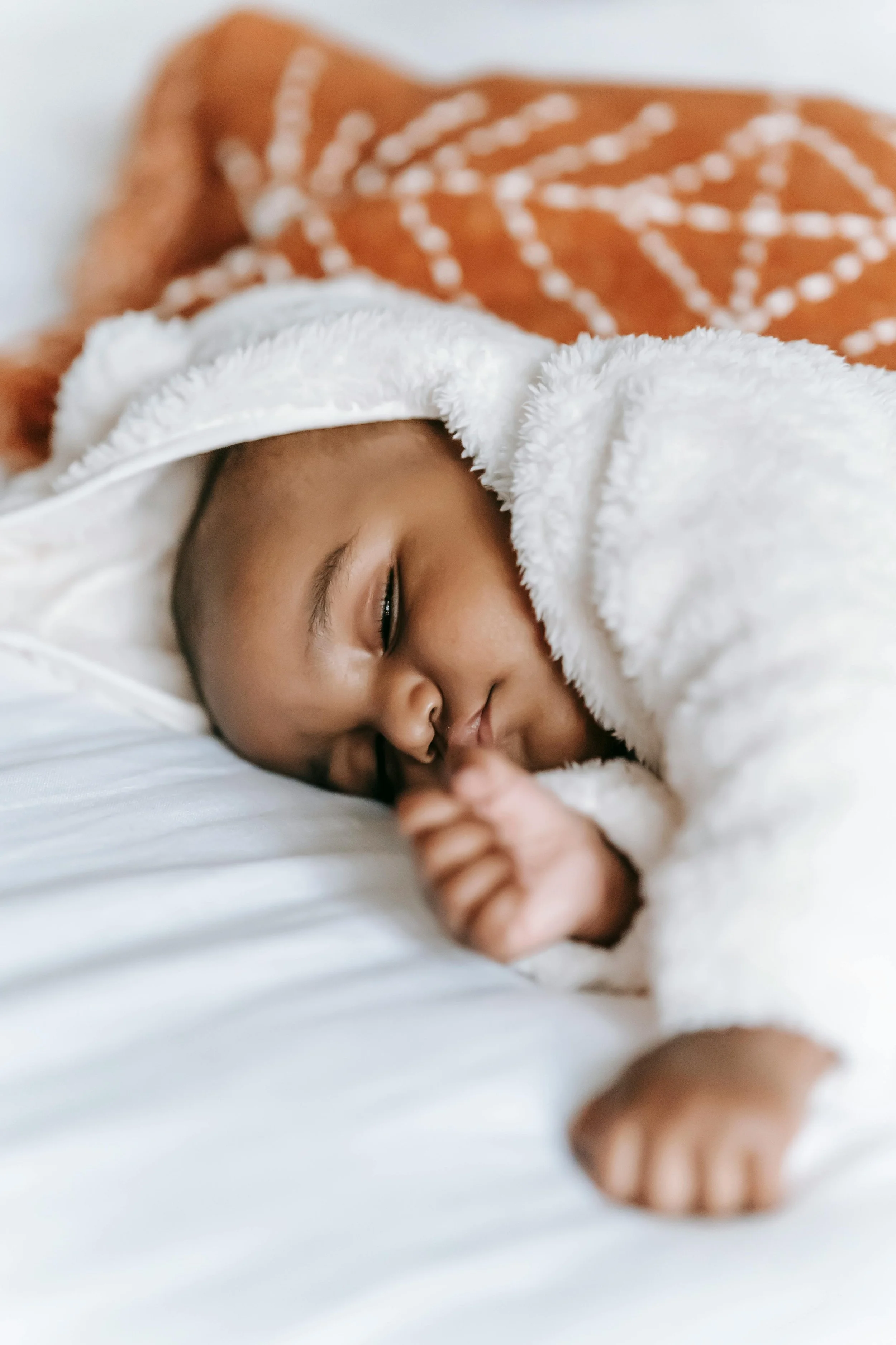 Close-up of a sleeping baby with a blanket partially covering their face, lying on white sheets.