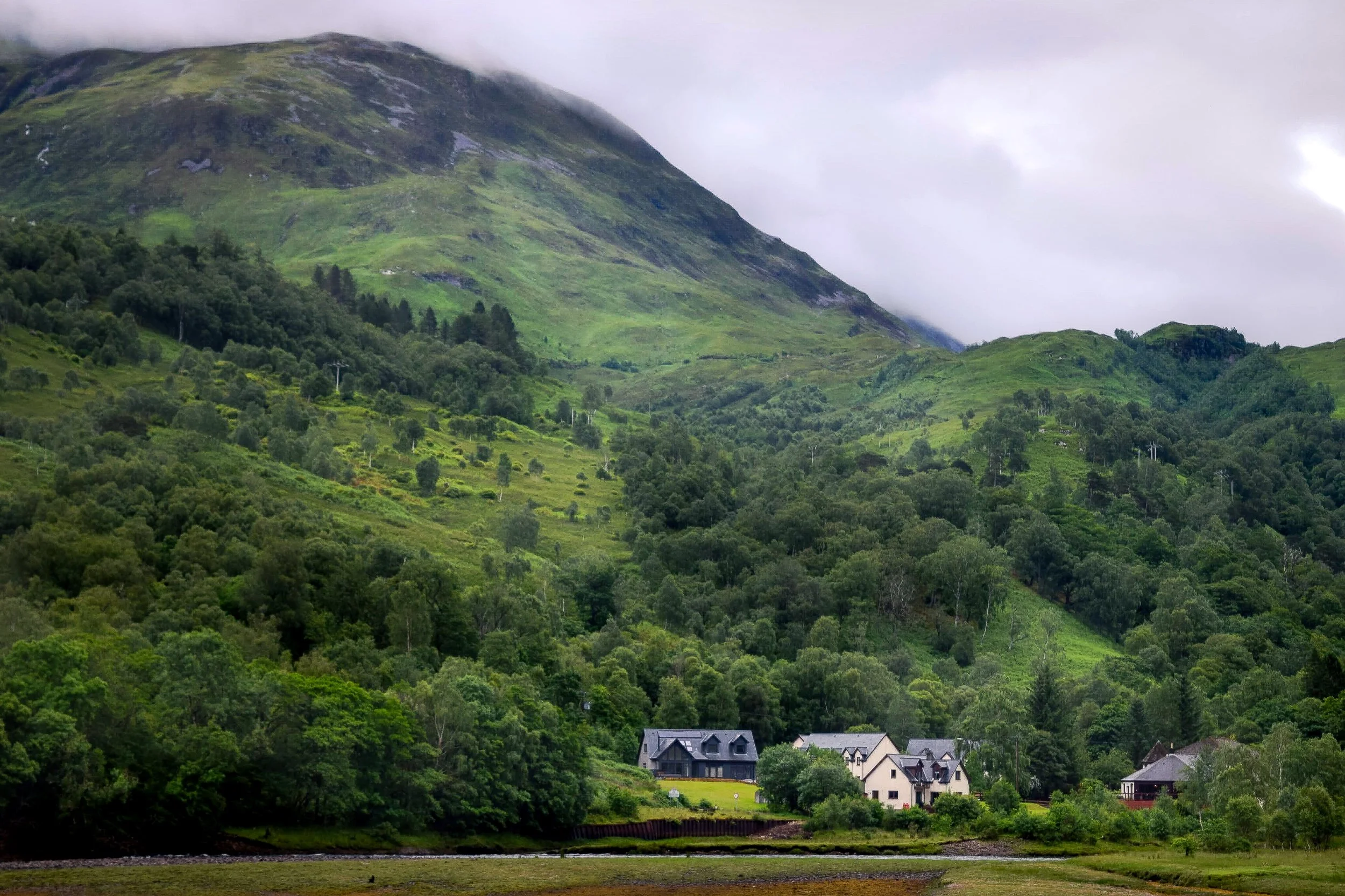 Lush green hills and mountains with scattered houses in a rural area, cloudy sky.