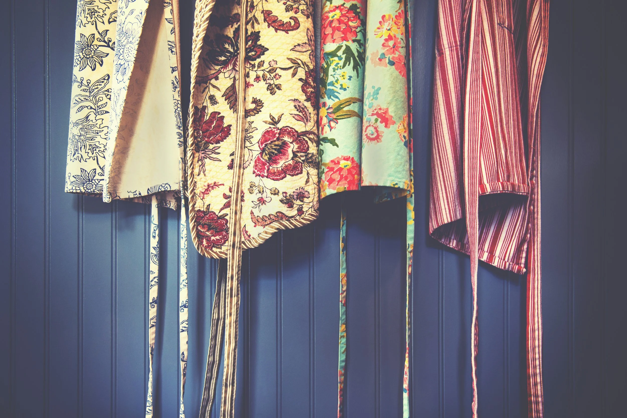 A collection of embroidered and patterned fabric strips hanging on a dark blue wall.