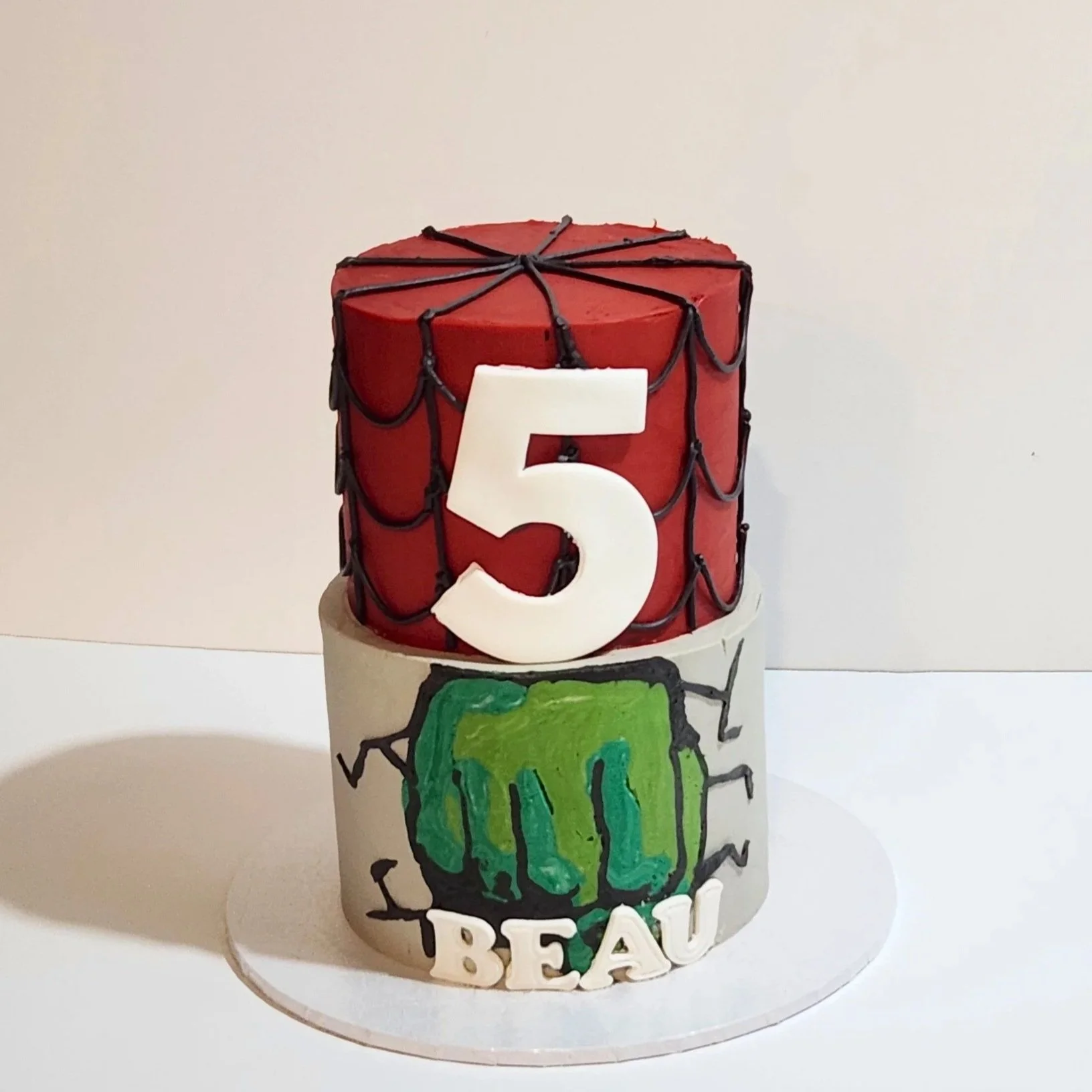 The top tier features a striking Spider-Man theme complete with a handcrafted fondant number 5 topper, while the bottom tier showcases a powerful Hulk inspired design with a dramatic Hulk fist punching through a textured steel grey background.