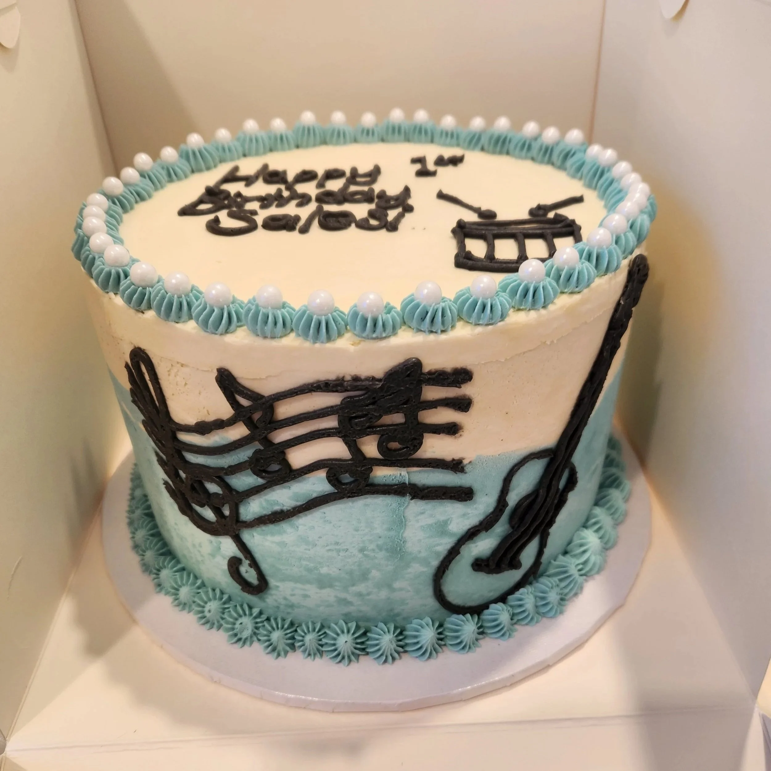 Soft blue and white musical themed first birthday cake made with banana cake layers, custom decorations and elegant handcrafted details for special celebrations.
