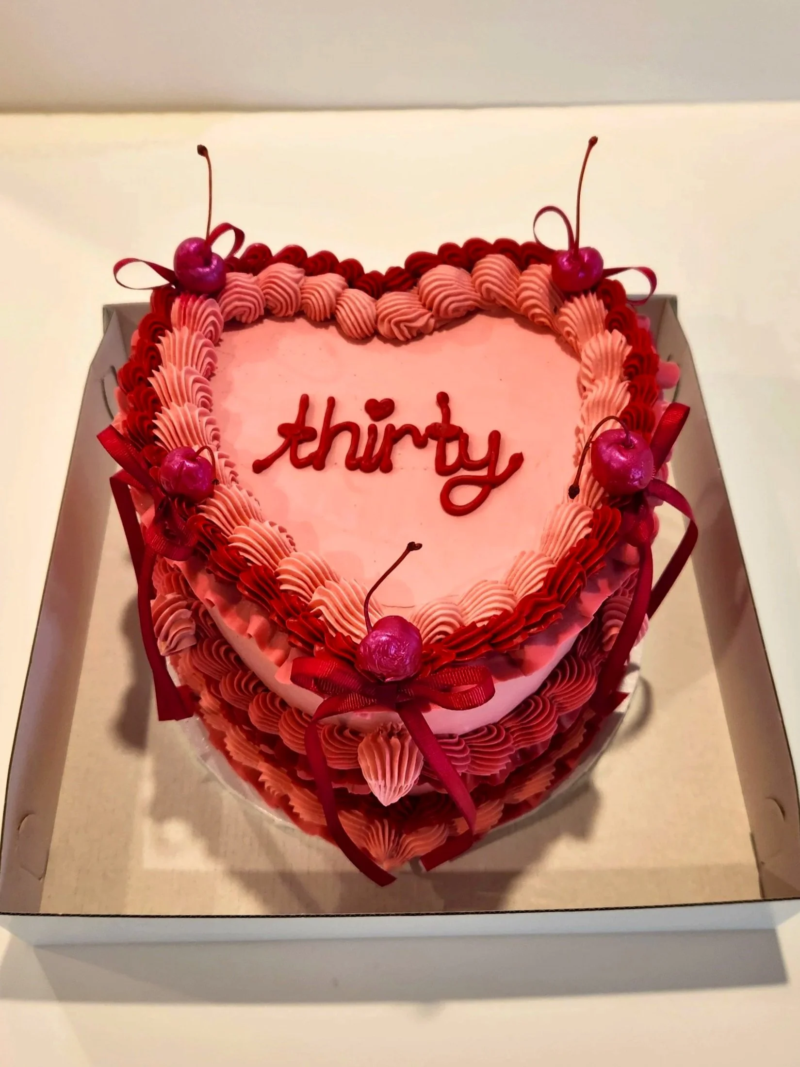 Vintage Heart-shaped pink birthday cake decorated with pink and red icing, cherries, and red ribbons, with a message that says 'thirty' on top.