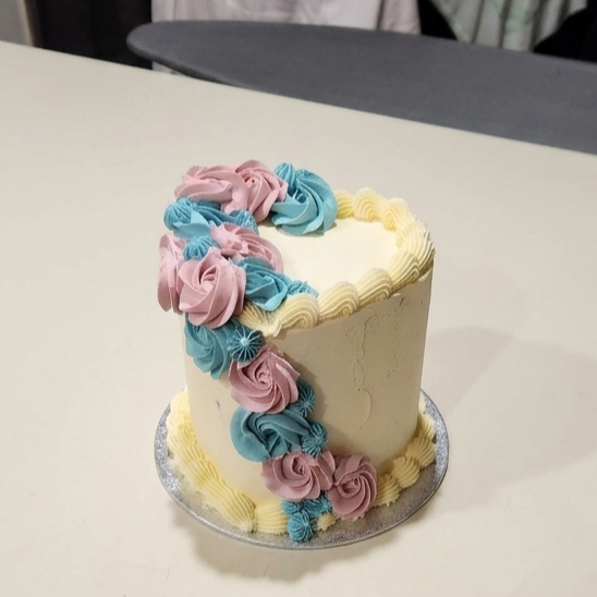 A celebratory cake decorated with pastel pink, blue, and yellow frosting flowers and borders on a white table.