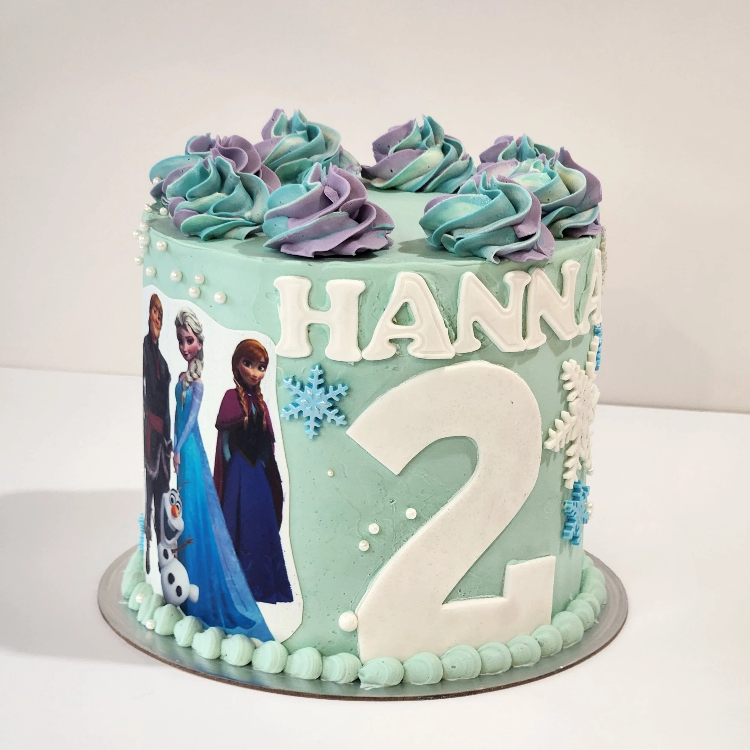A 6-inch Frozen-themed cake finished in soft blue tones with smooth buttercream, delicate snowflake details, and themed toppers. A magical design perfect for any Frozen fan.