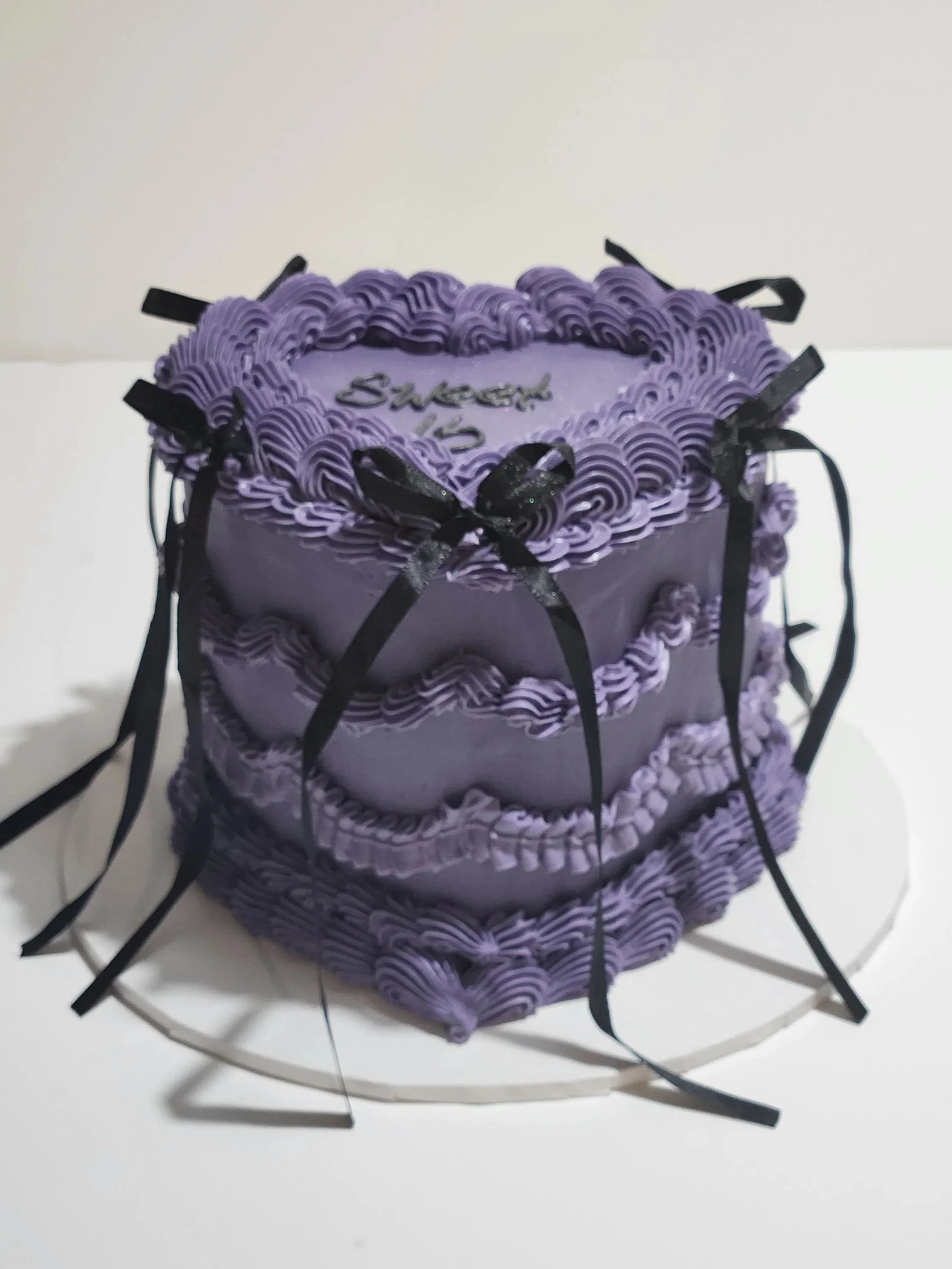 Vintage Heart Purple birthday cake with purple buttercream, black ribbons, and the words 'Sweet 16' written on top. The cake is decorated with purple and black accents.