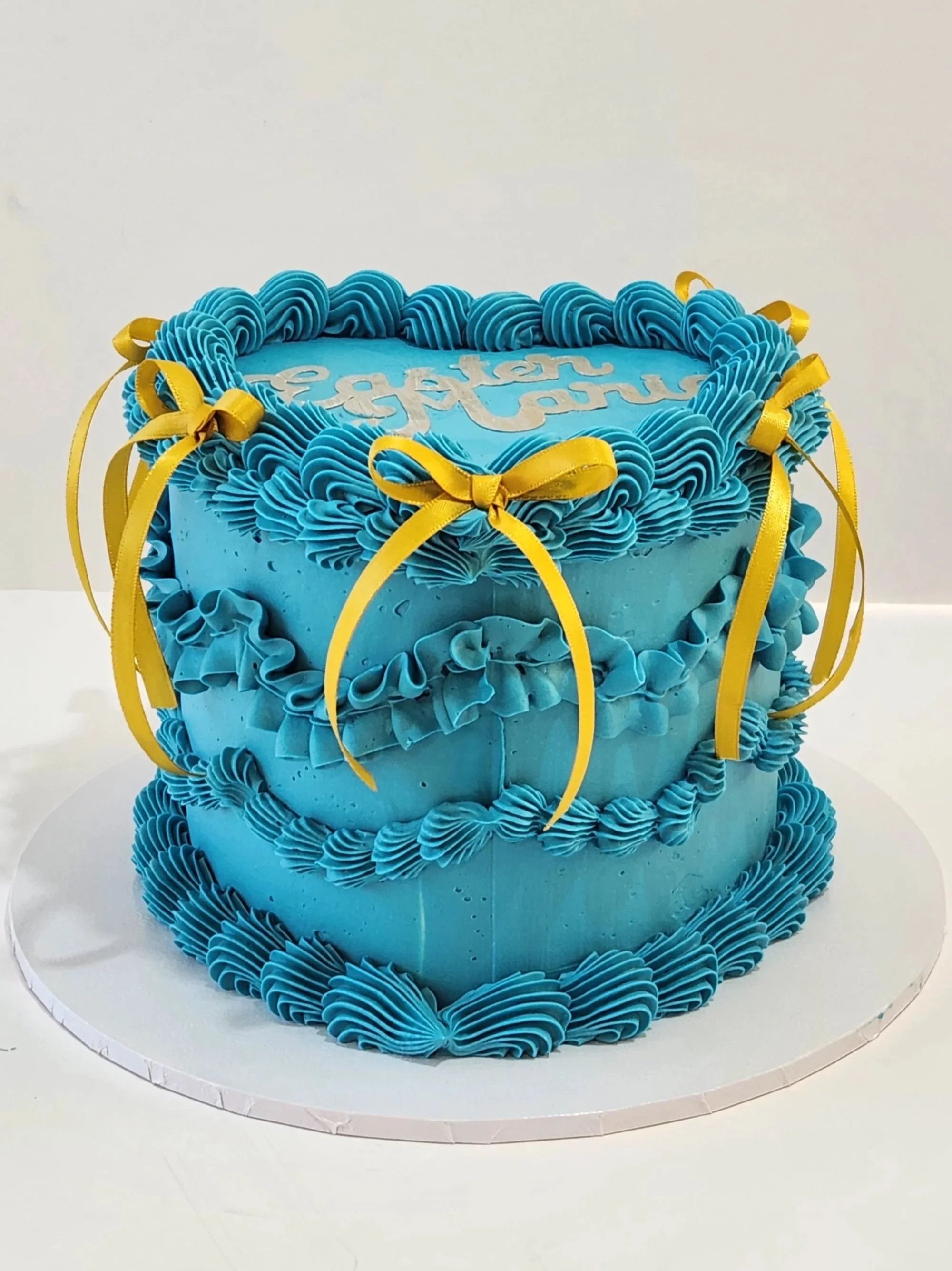 A vintage-heart celebration cake with light blue buttercream, with butter-yellow ribbon.