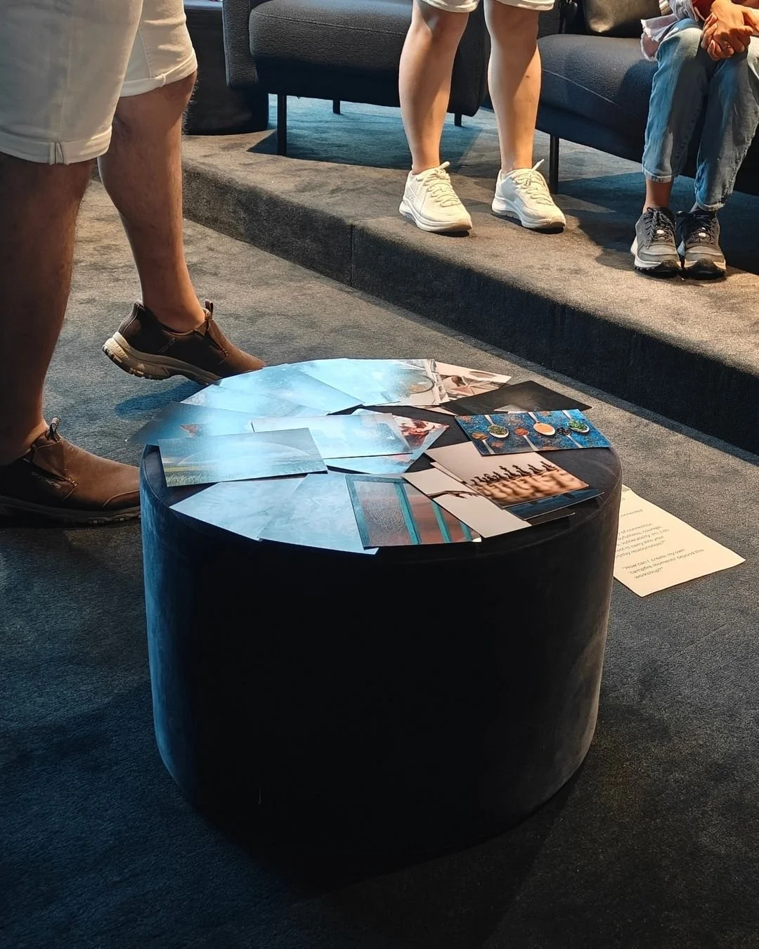 People gathered around a black round table displaying various photographs and printed materials in an indoor setting.