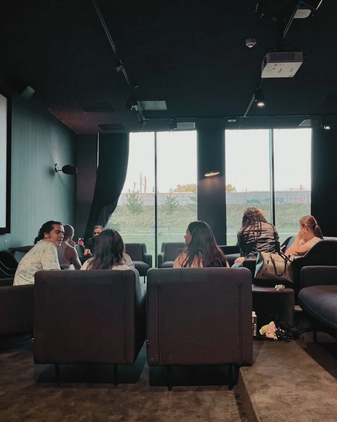 People sitting and talking with each other, sitting on armchairs in a dark room.