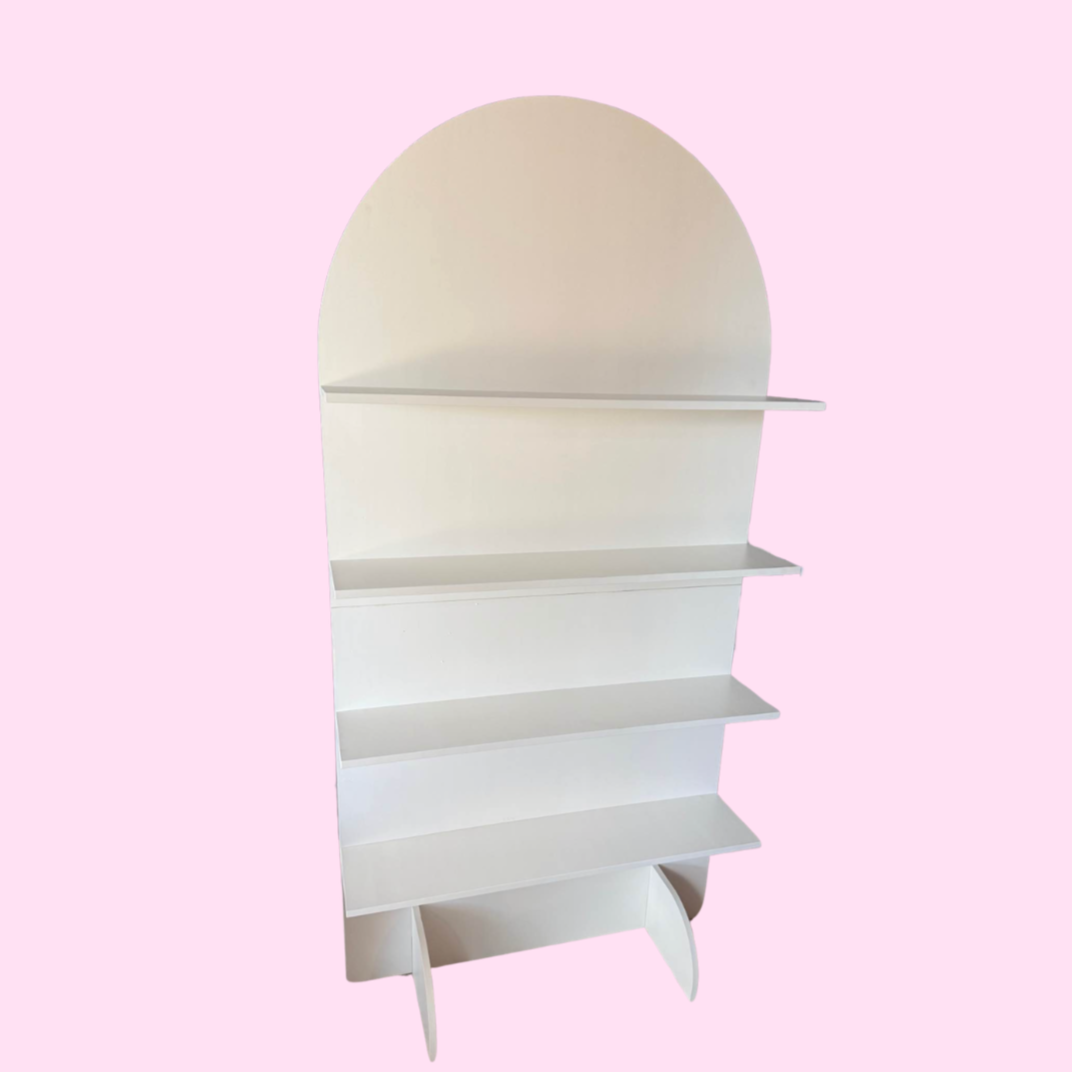White bookshelf with a rounded top and fin-shaped legs, set against a pink background.