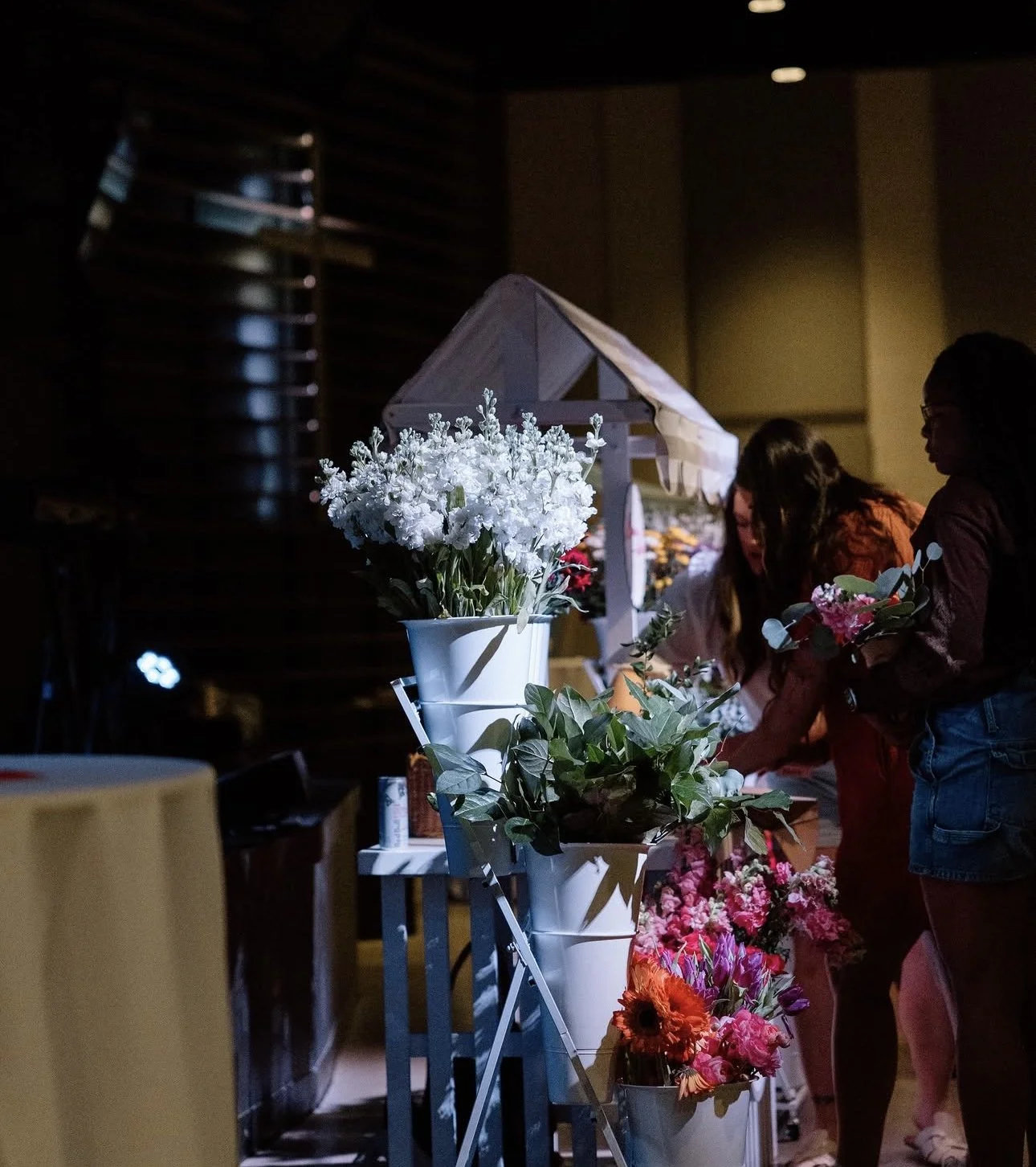 People shopping for flowers at an indoor floral market with various colorful blossoms on display.