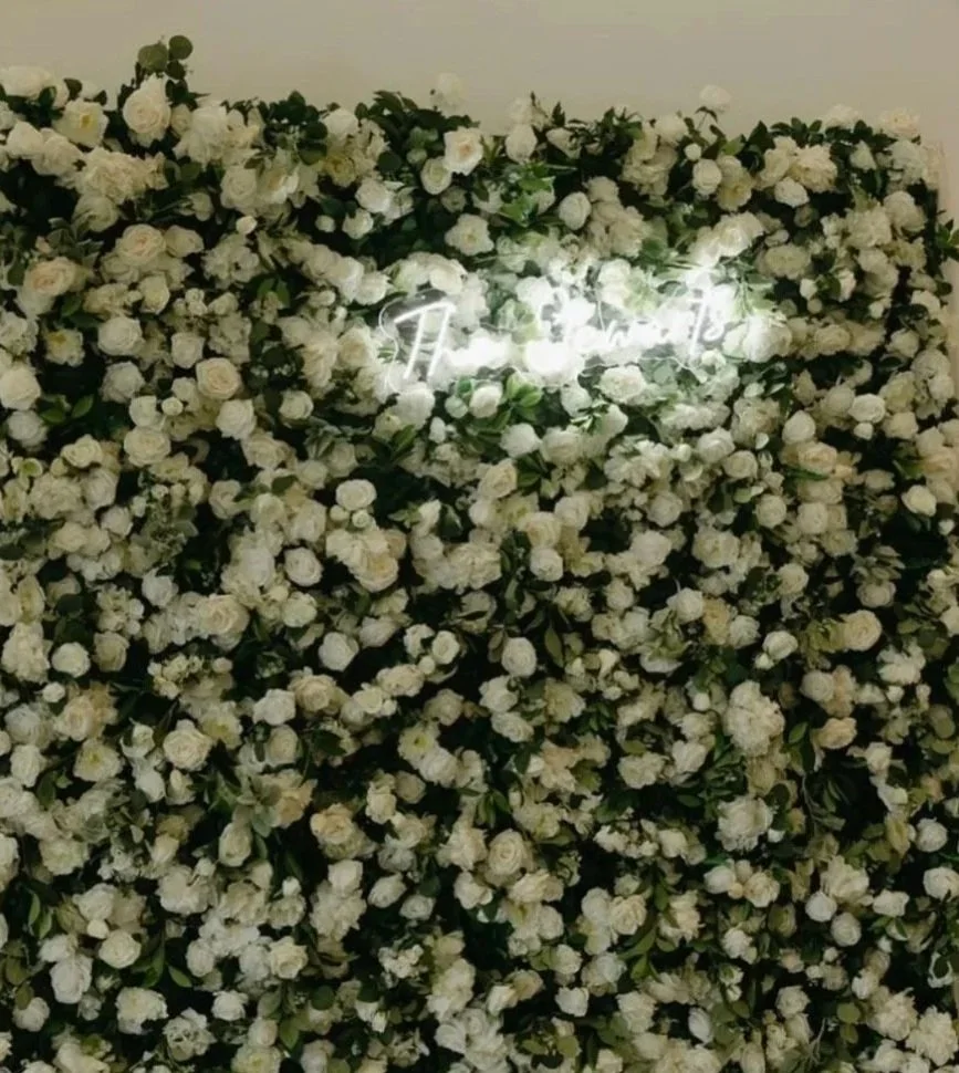 Wall decorated with white roses and green leaves, with a glowing neon sign spelling 'Tiffany' in the center.