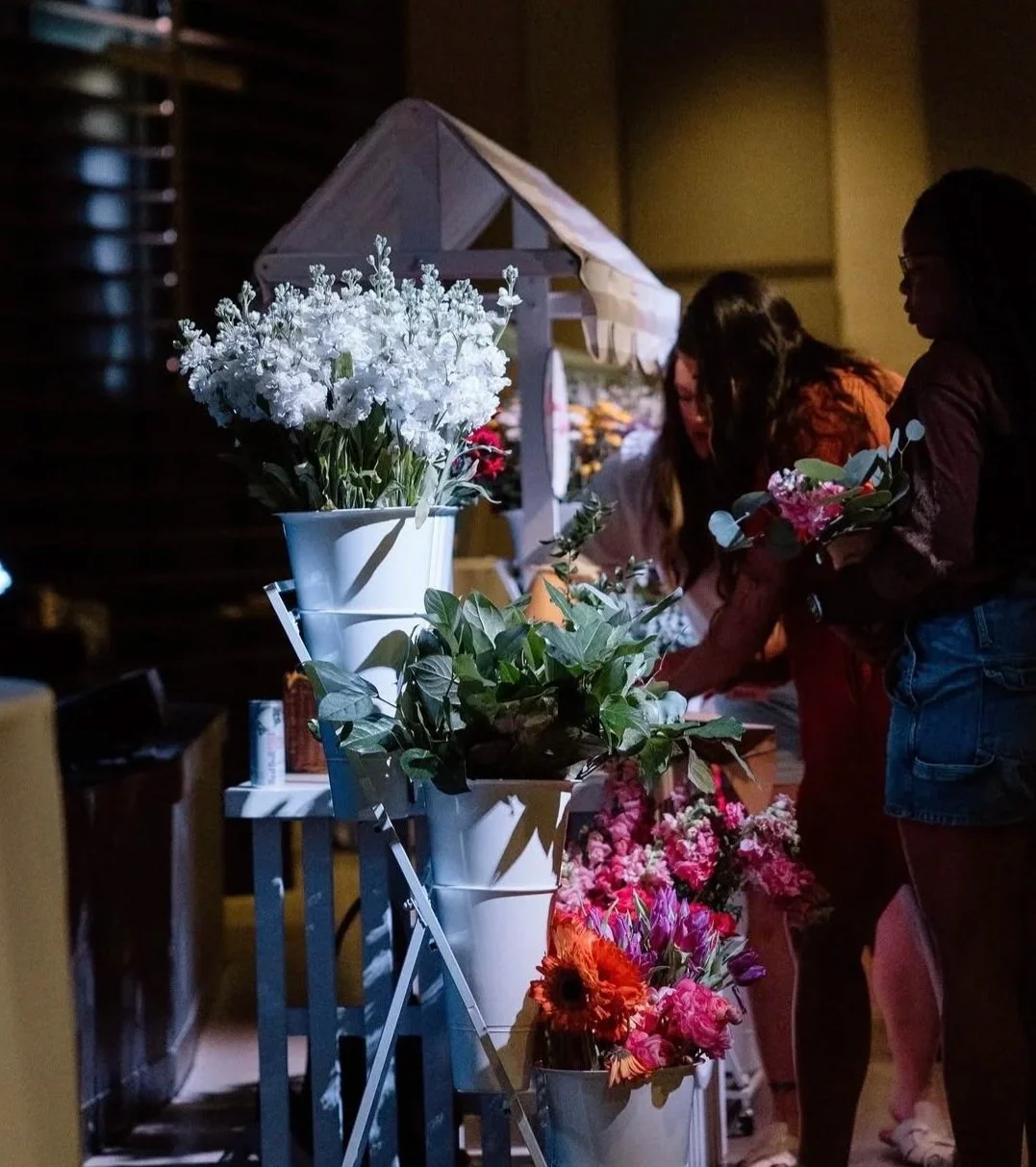 People shopping for flowers at a floral stand with colorful flowers on display at night.