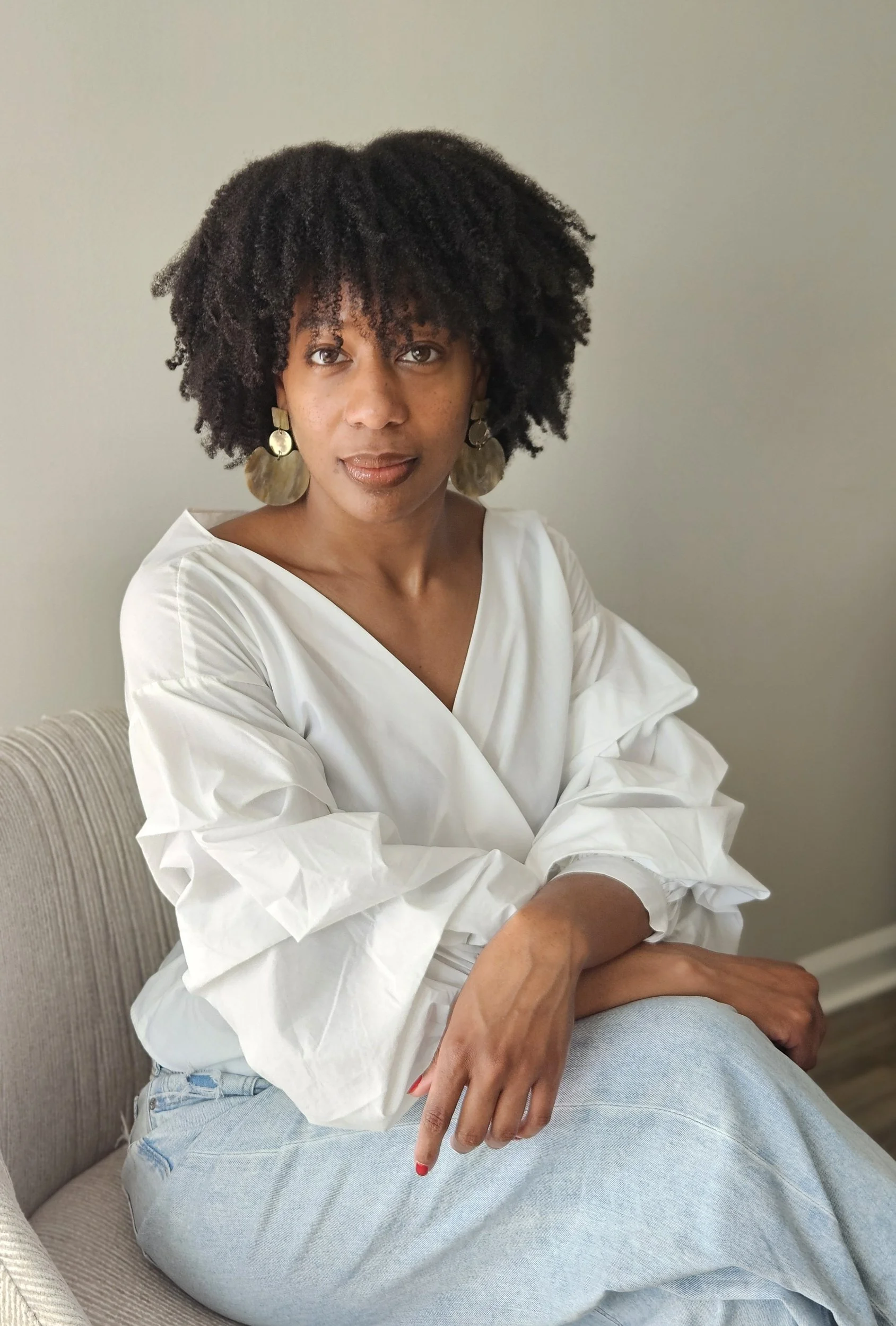 Woman wearing blue jeans and white shirt sitting in chair.