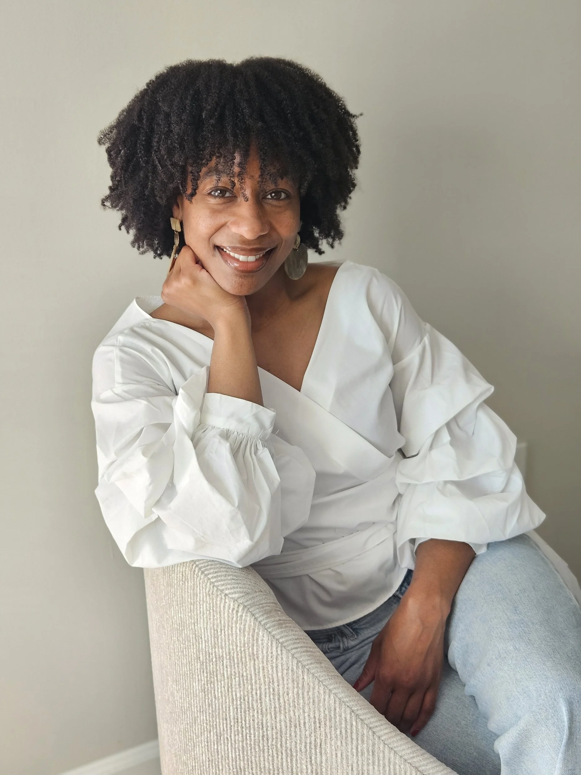 Woman wearing blue jeans and white shirt sitting in chair.
